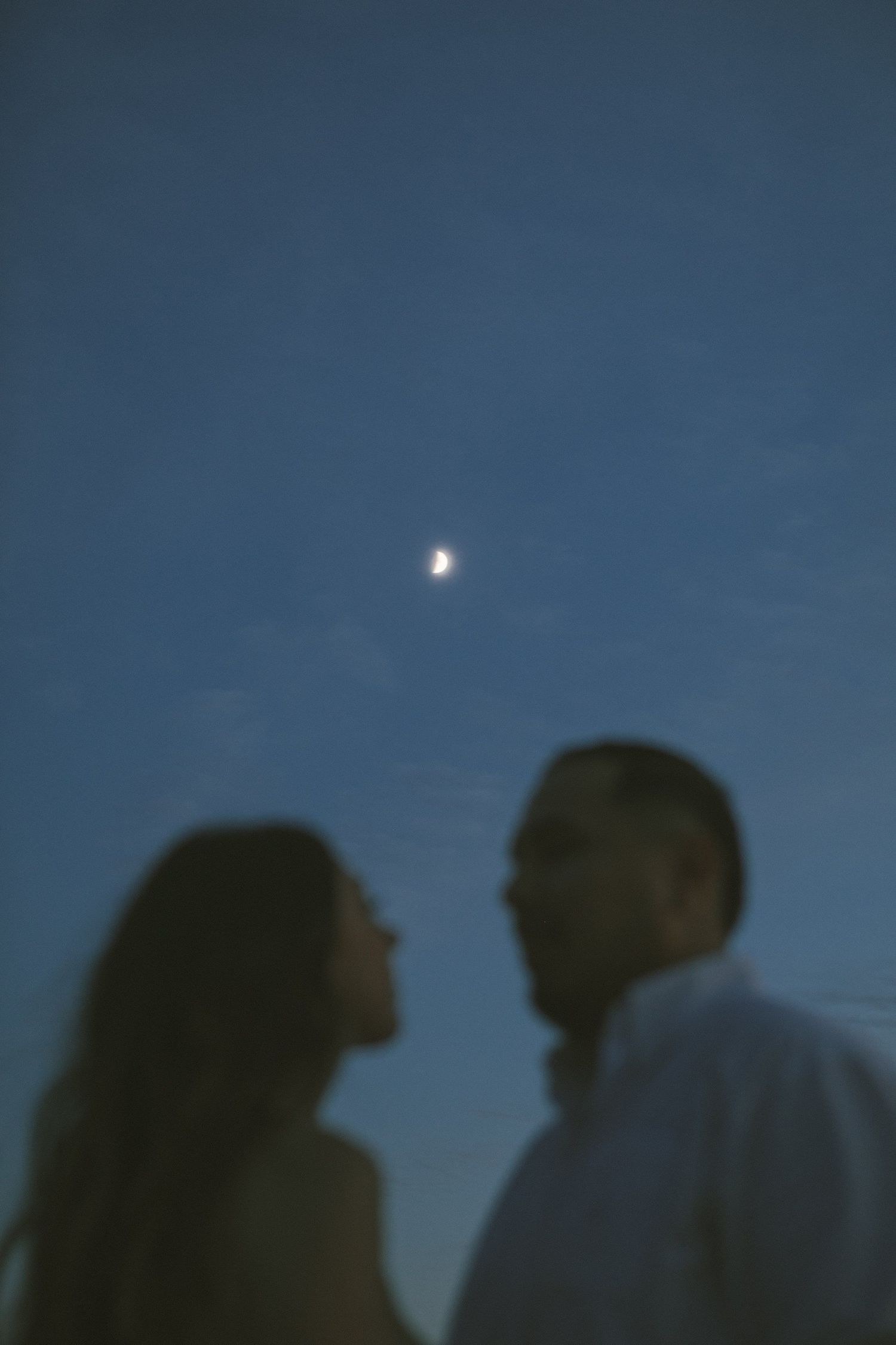 Silhouetted figures against deep blue evening sky with visible moon.