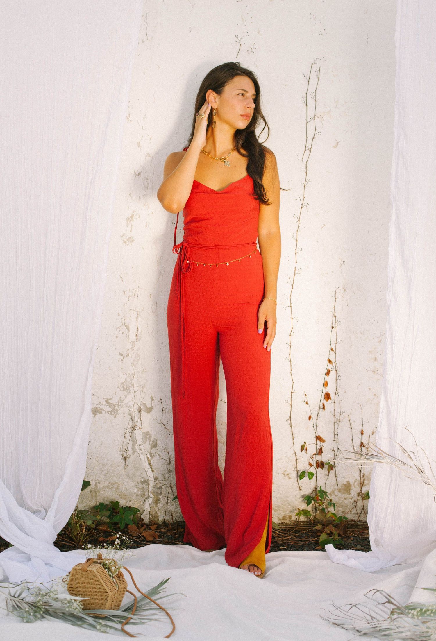 Fashion series showing a red jumpsuit outfit against a white wall background.