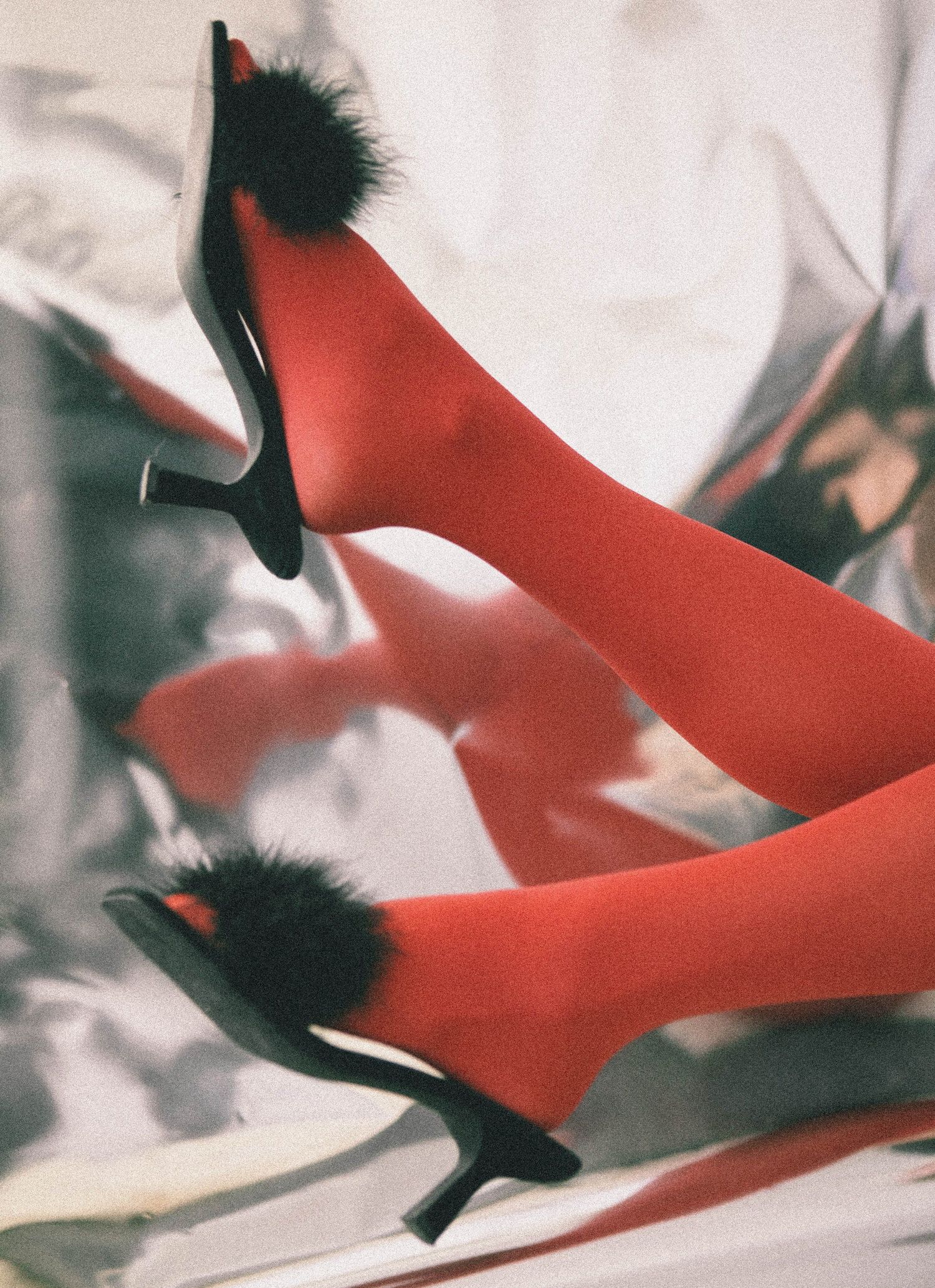 Artistic close-up of red high heels with black feather details.