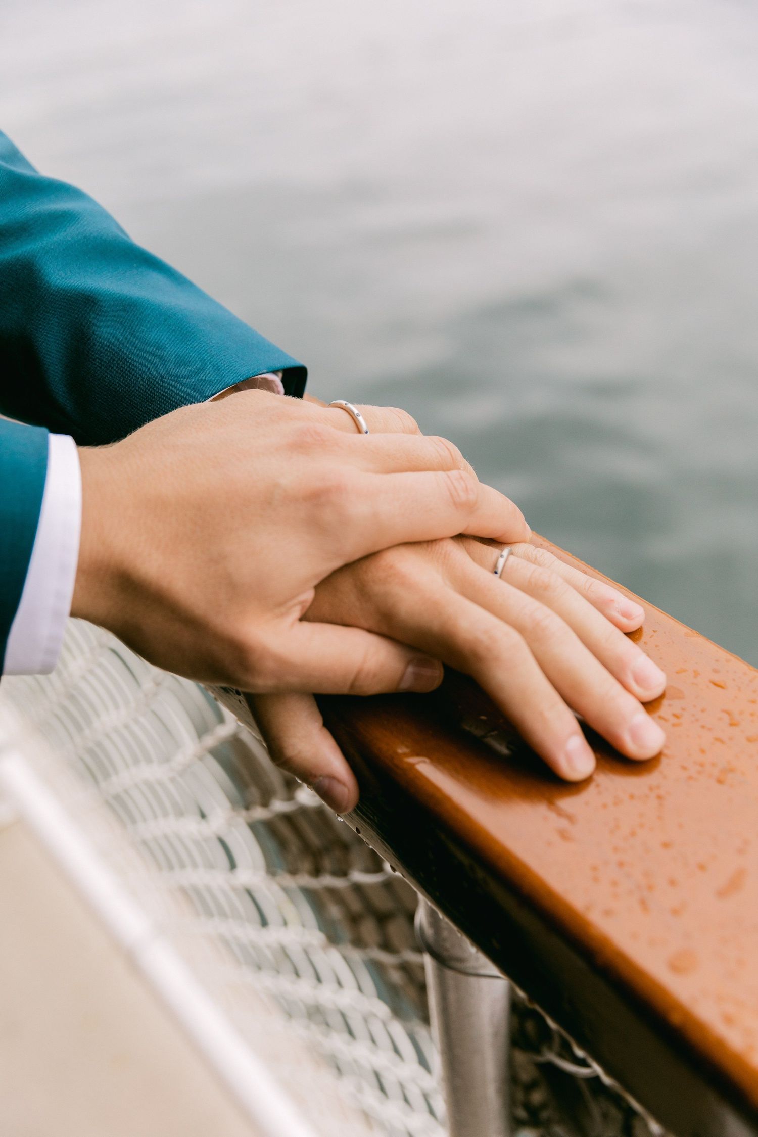 Close-up of hands resting on a wooden railing with water in the background.