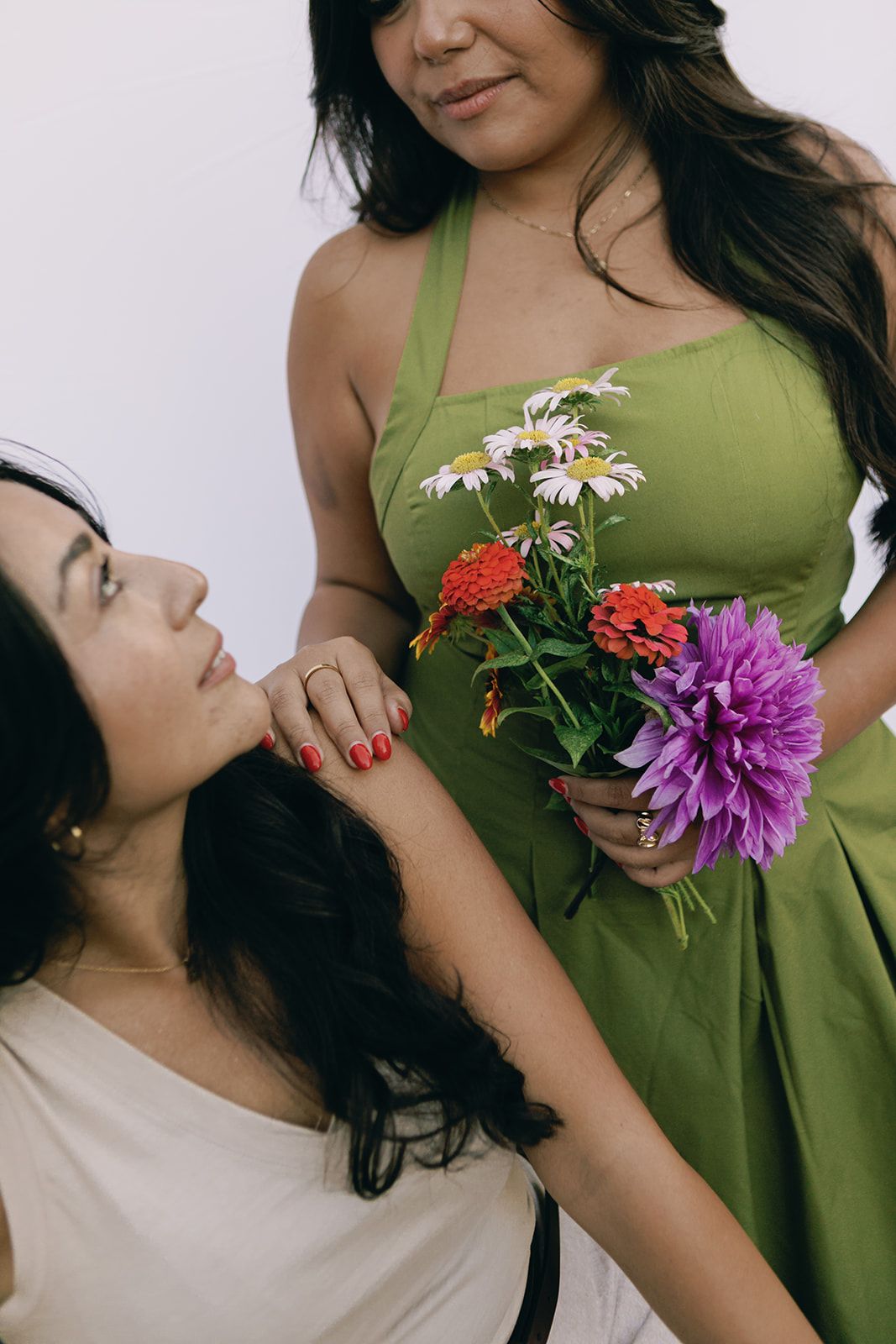 Two people in casual attire share a tender moment with colorful flowers including daisies and a purple dahlia.