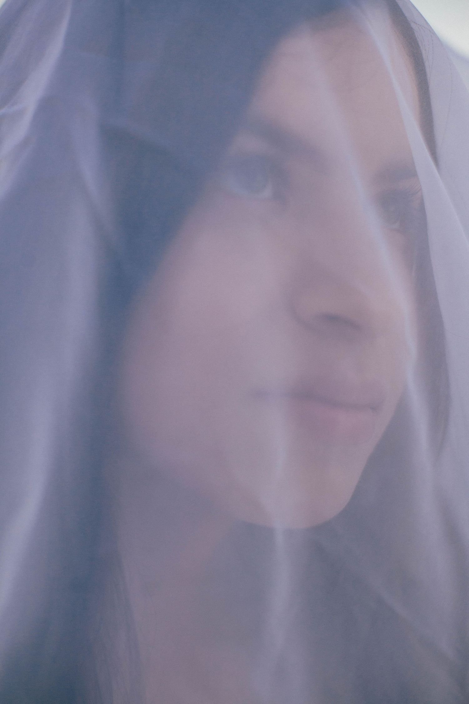 Ethereal portrait through sheer white fabric creating a dreamy effect.