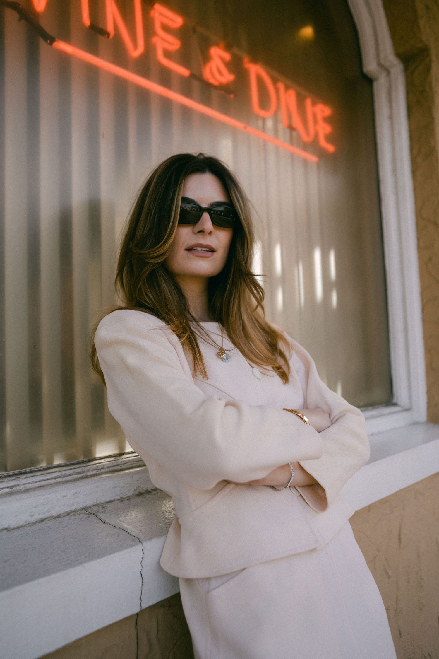 A person in a white oversized blazer poses against a wall with neon signage in a series of four stylish photos.