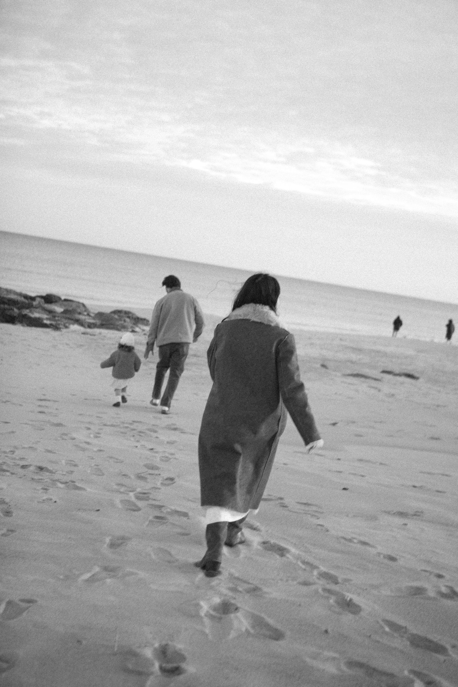 Black and white photo of people walking along a beach shoreline.