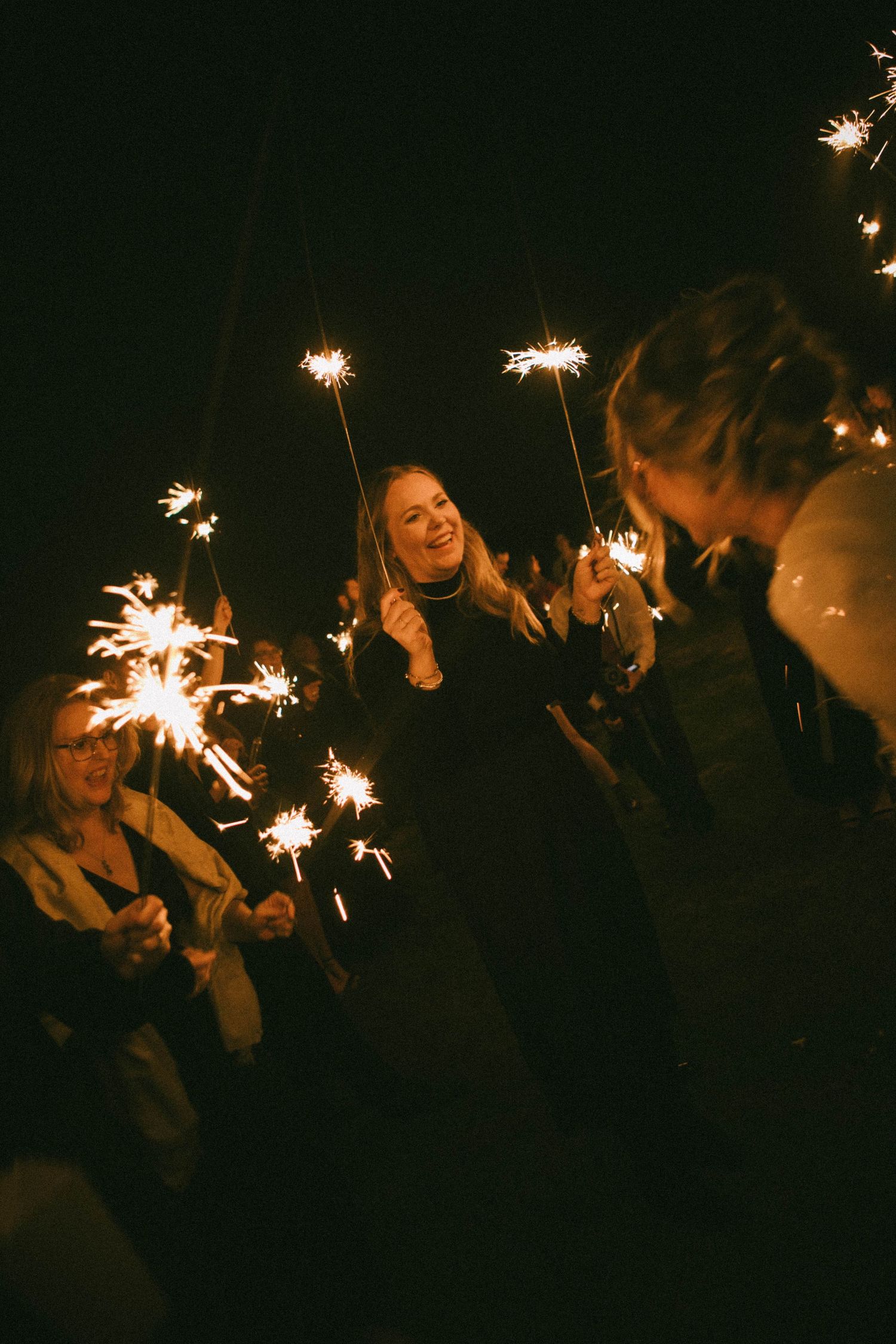 Guests hold sparklers creating a magical nighttime atmosphere at a wedding celebration.