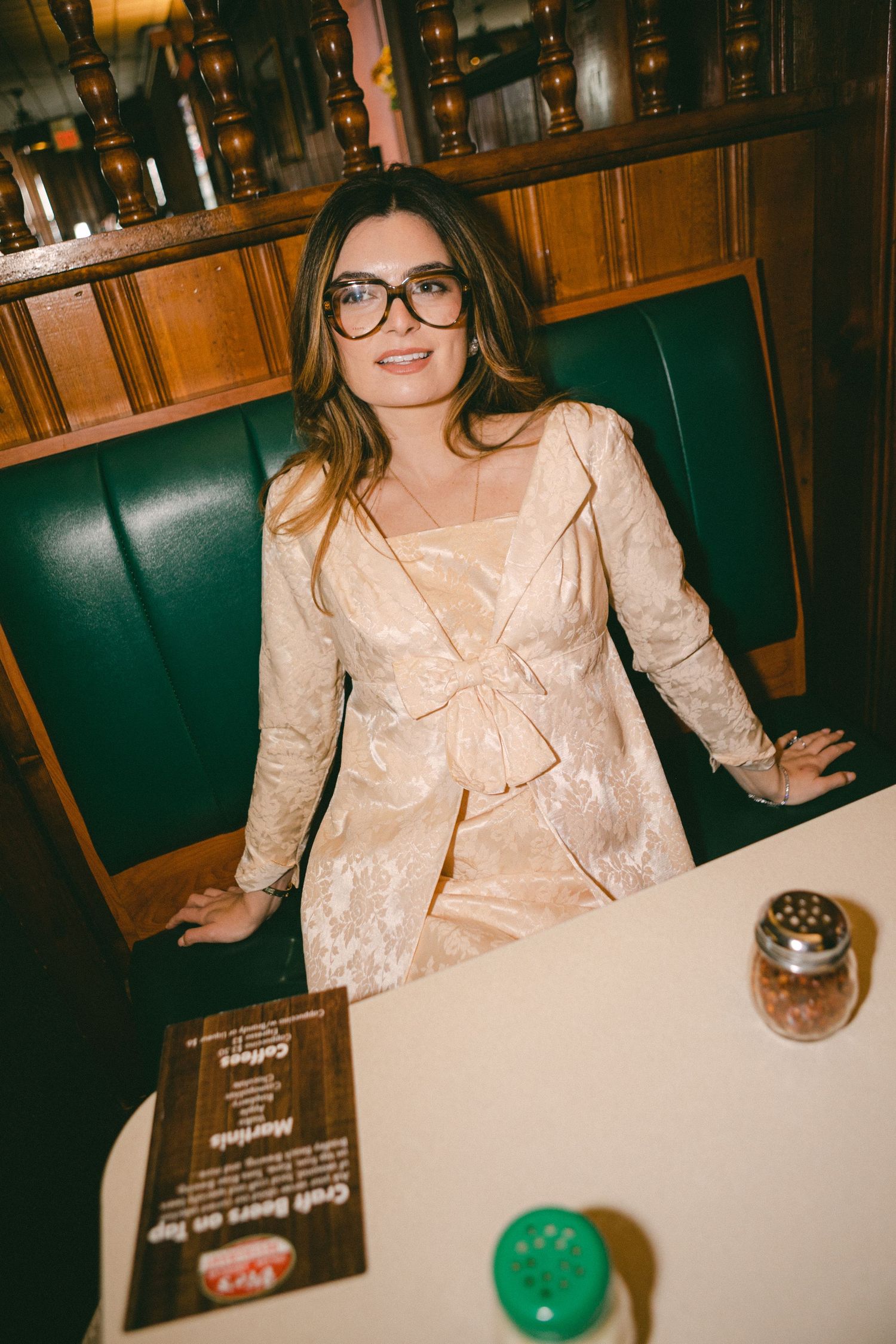 Person in a peach-colored dress sits at a restaurant table with a dark wooden interior and menu visible.
