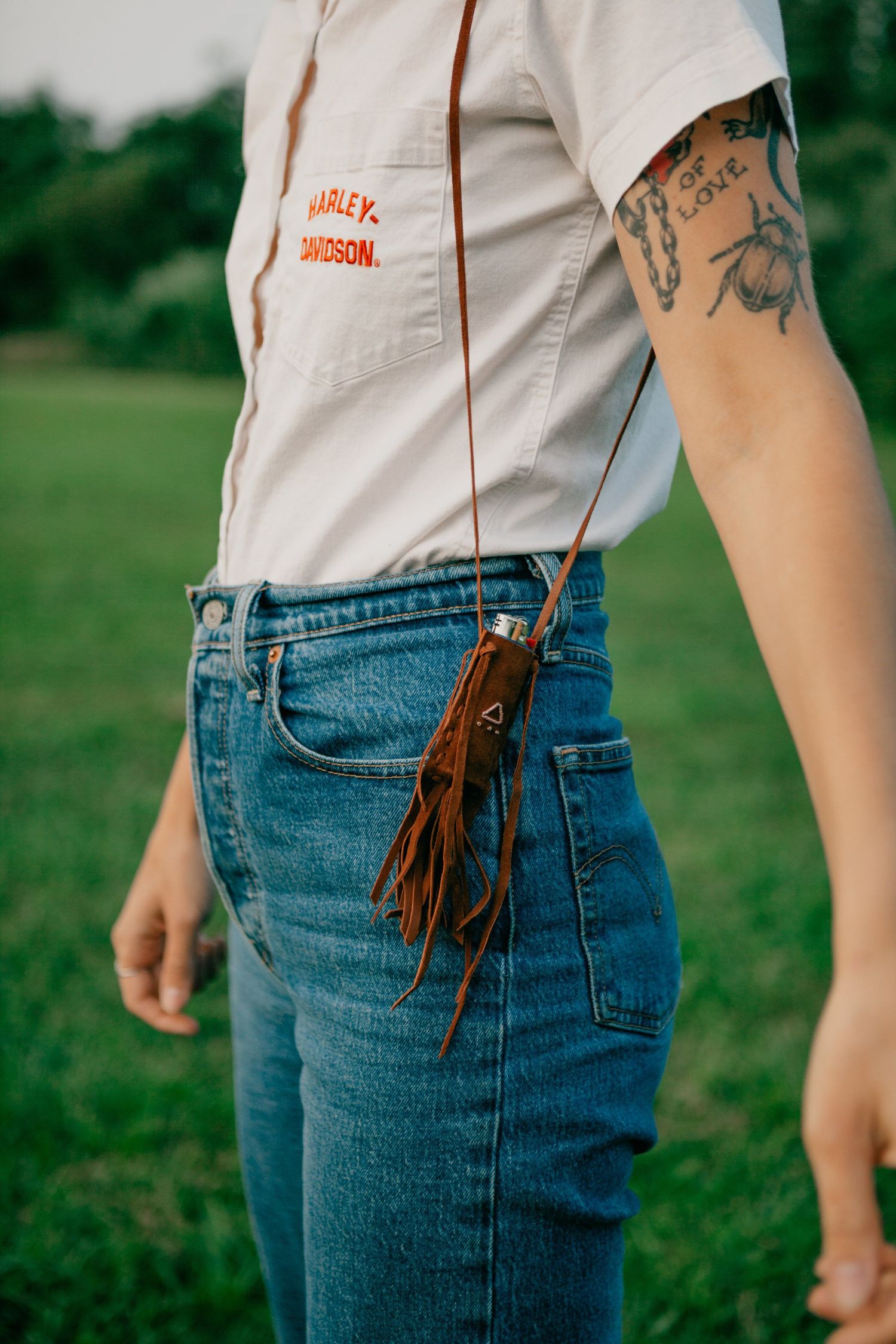 Close-up of denim jeans with leather fringe detail against green grass.