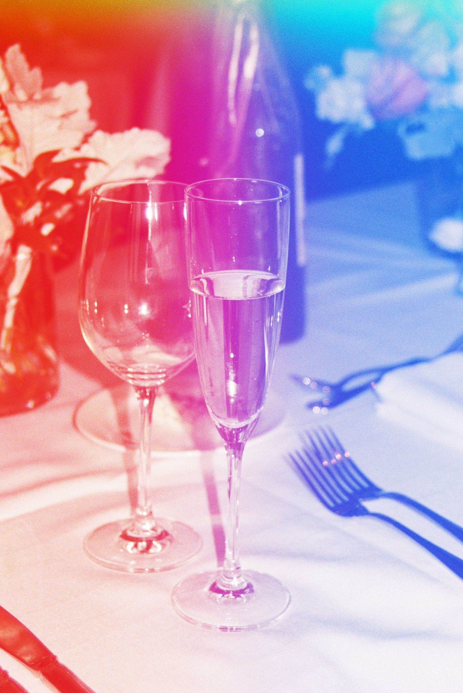 Elegant place settings with wine glasses on a white tablecloth illuminated by colorful lighting.