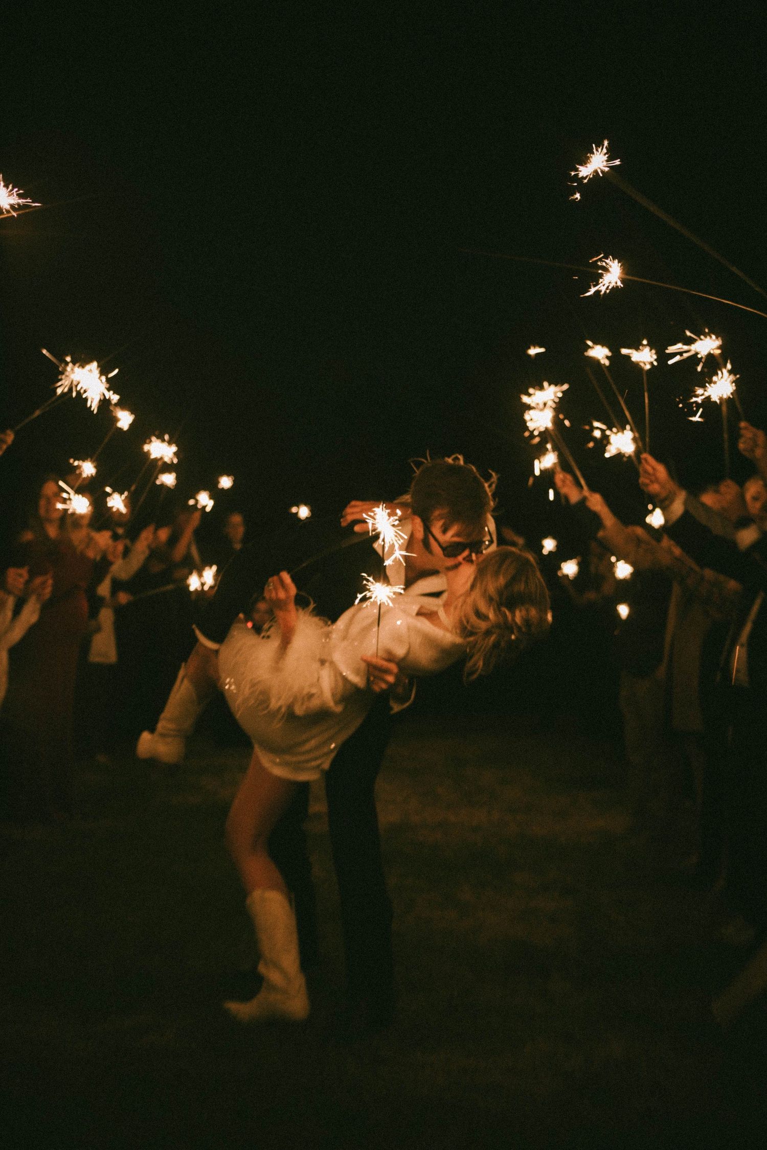 Wedding guests holding sparklers creating a magical nighttime celebration atmosphere.