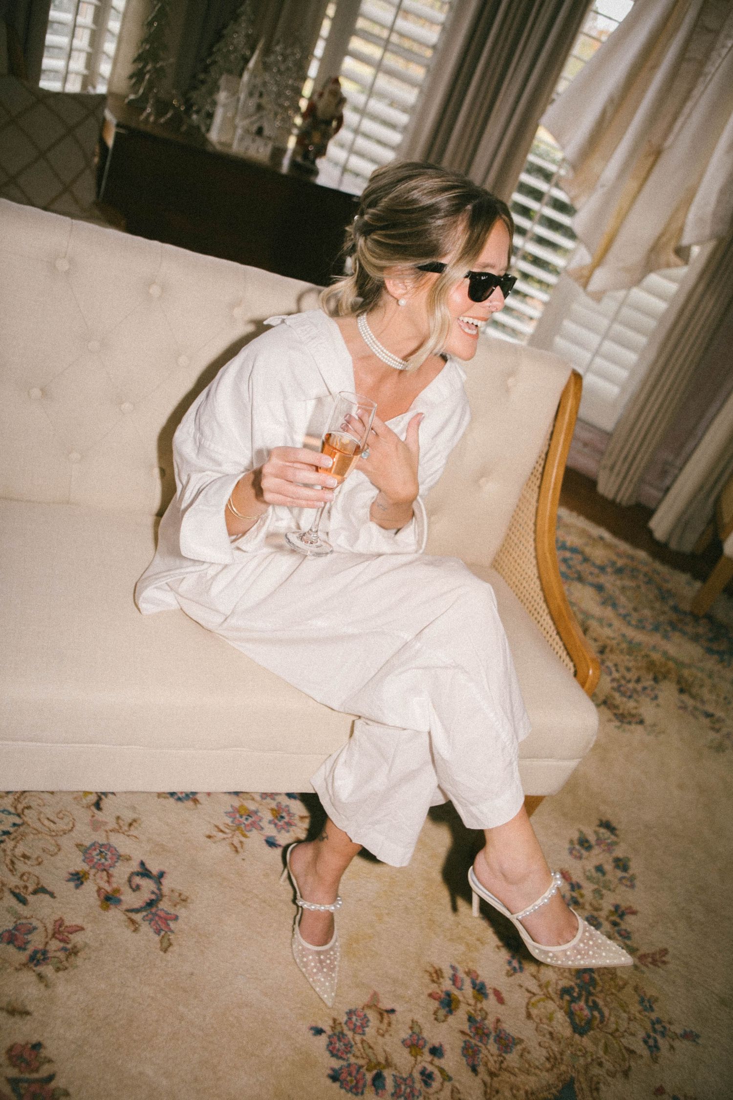 Person in white robe sitting on floral carpet drinking from a mug.