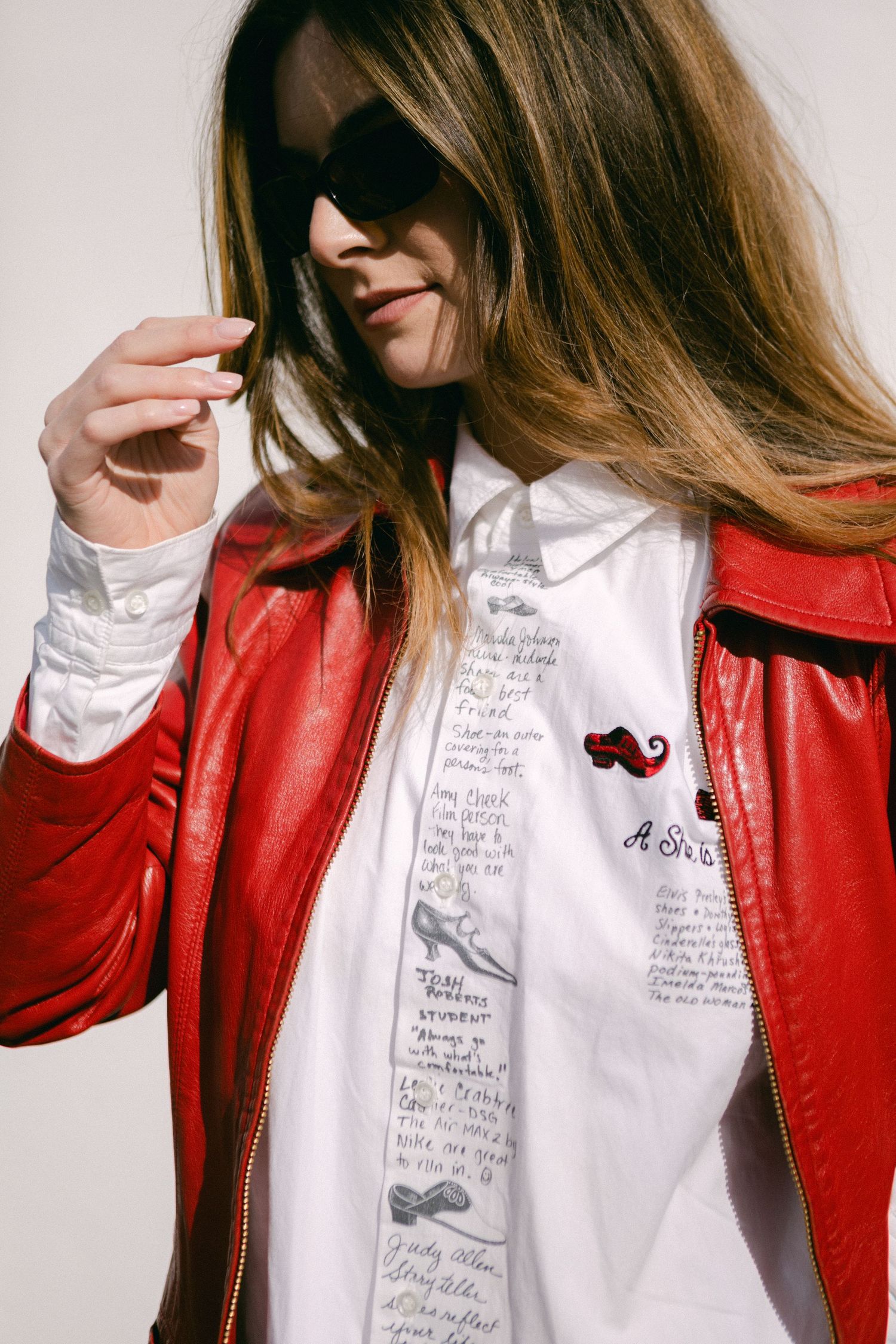 Person wearing red leather jacket and white shirt with handwritten text stands against white background.