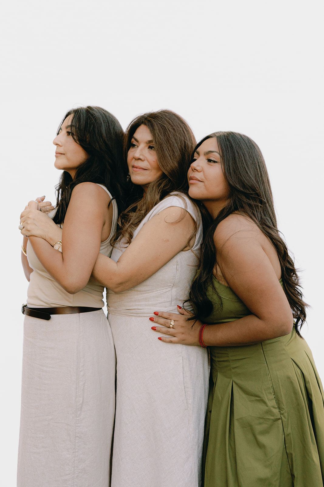 Three women in casual dresses embrace in a warm group hug against a white background.