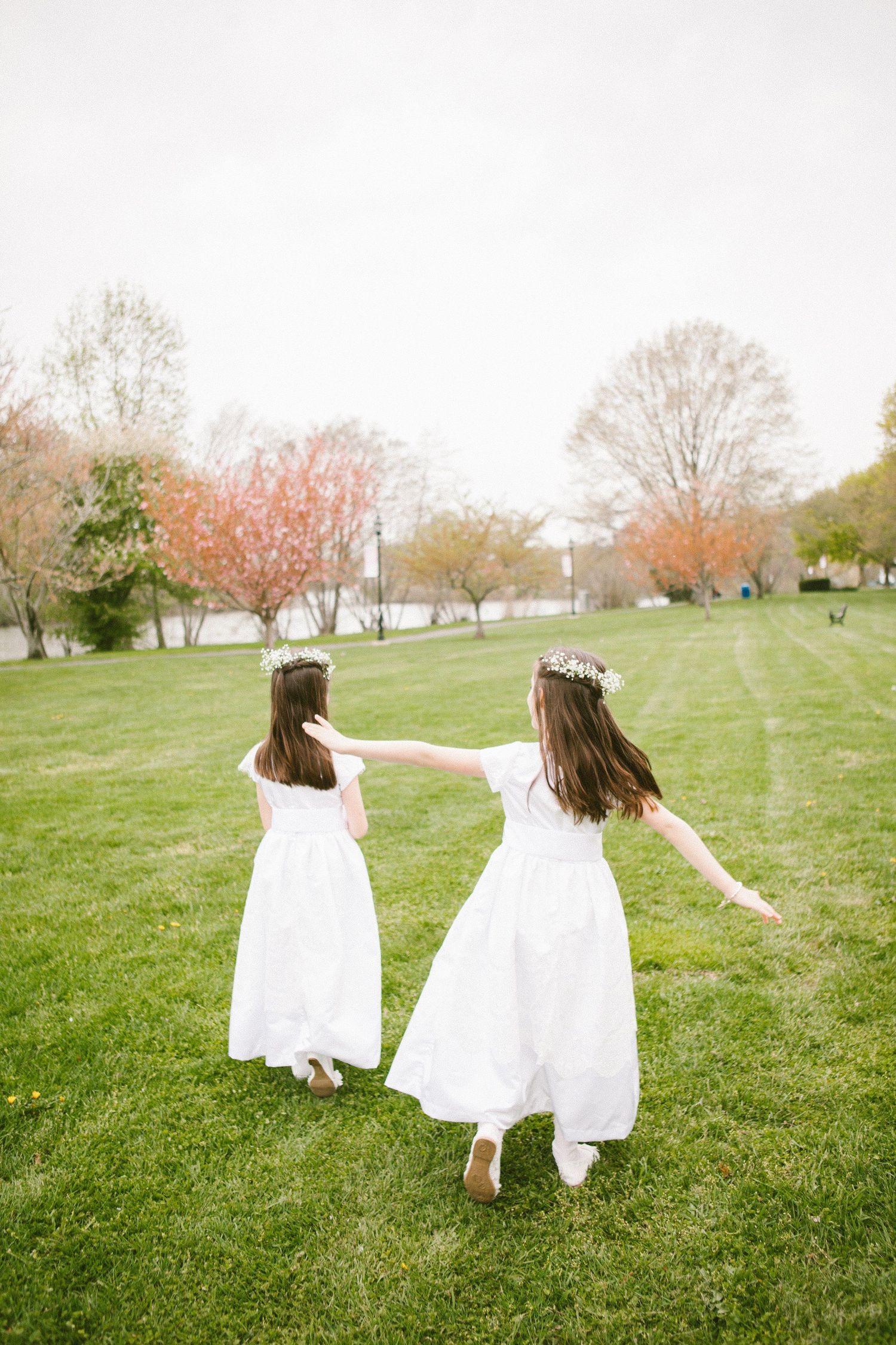 Two figures in white dresses running through a spring field with blooming trees.