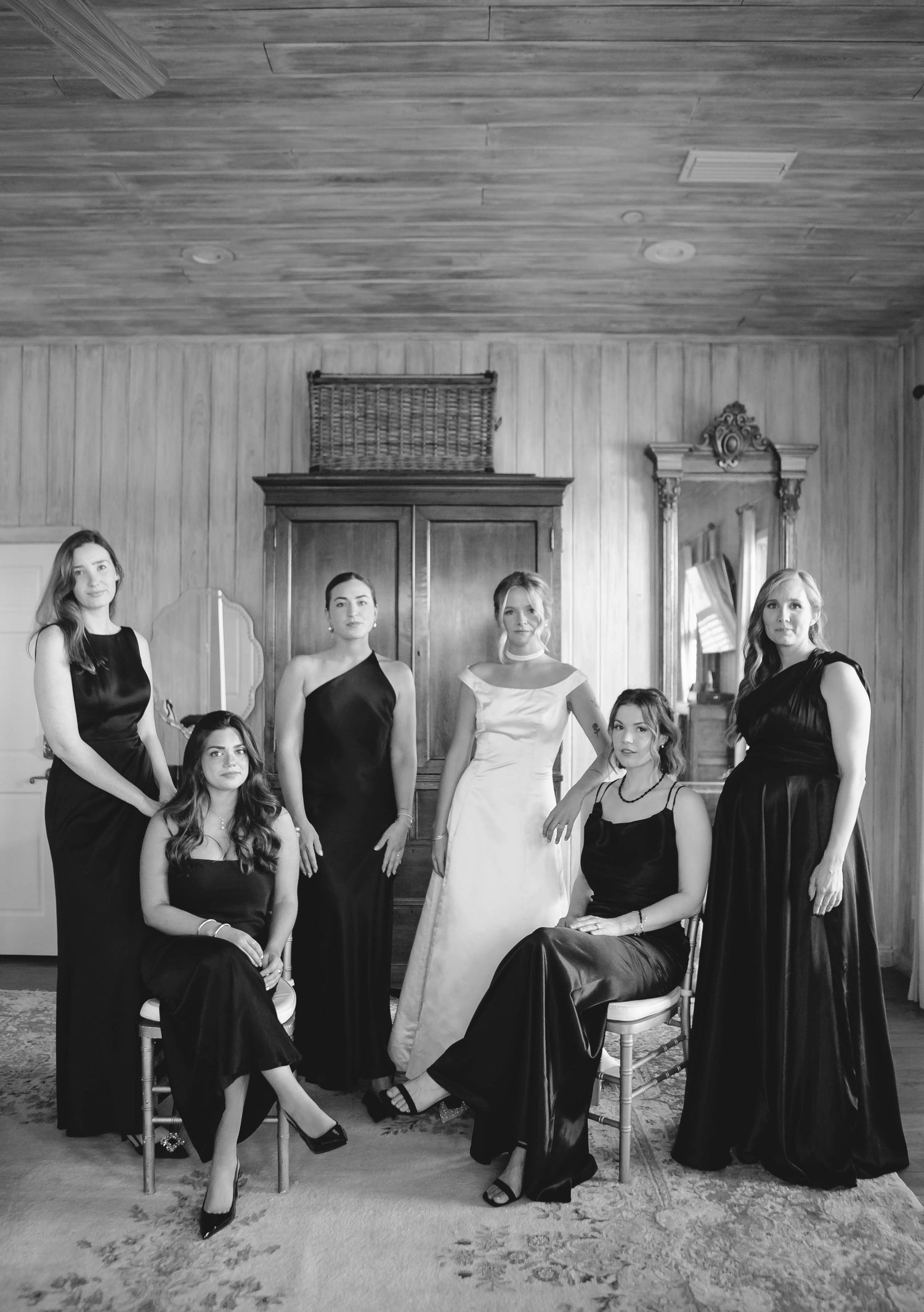 Wedding party in black dresses poses in a rustic wooden room.
