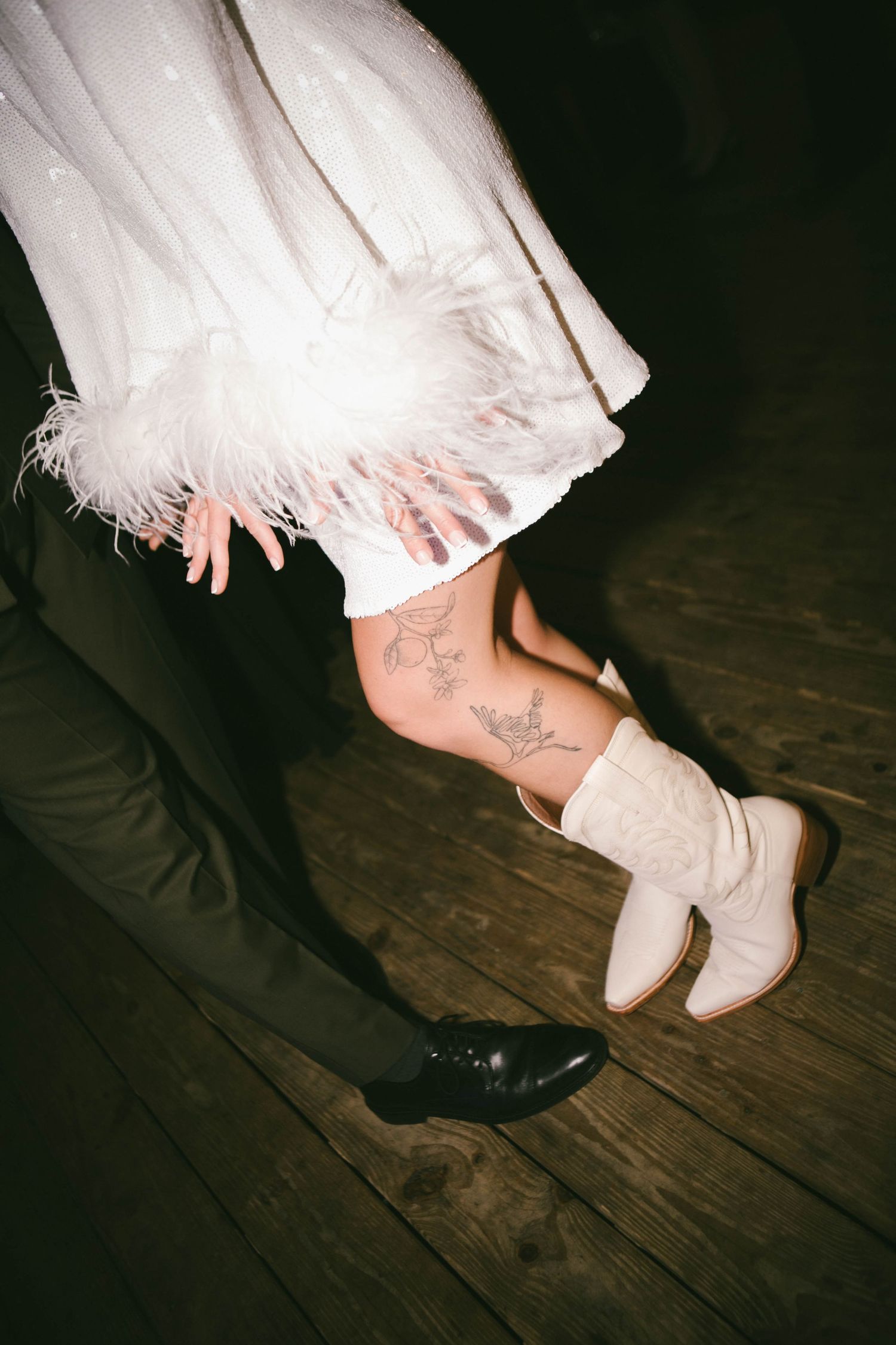 Close-up of wedding shoes showing a white bridal heel and black groom's shoe on wooden floor.