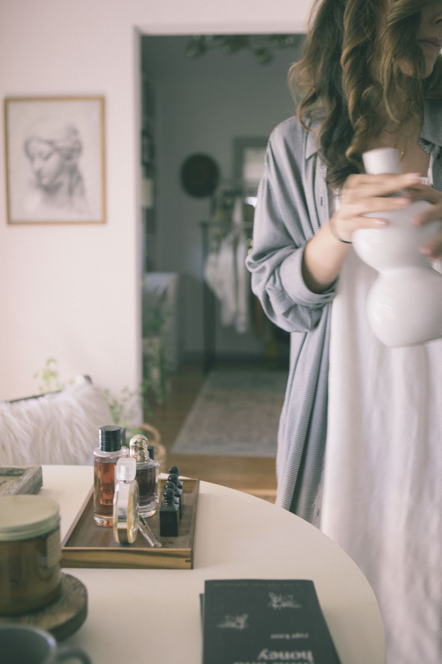 Person in gray sweater holding white ceramic mug in minimalist interior setting.