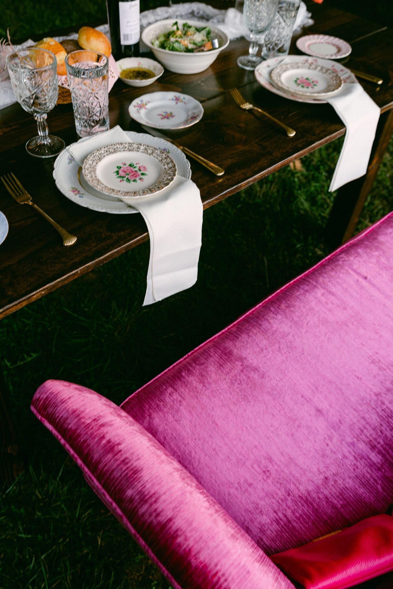 Elegant table setting with floral china plates, crystal glasses and pink velvet chair.