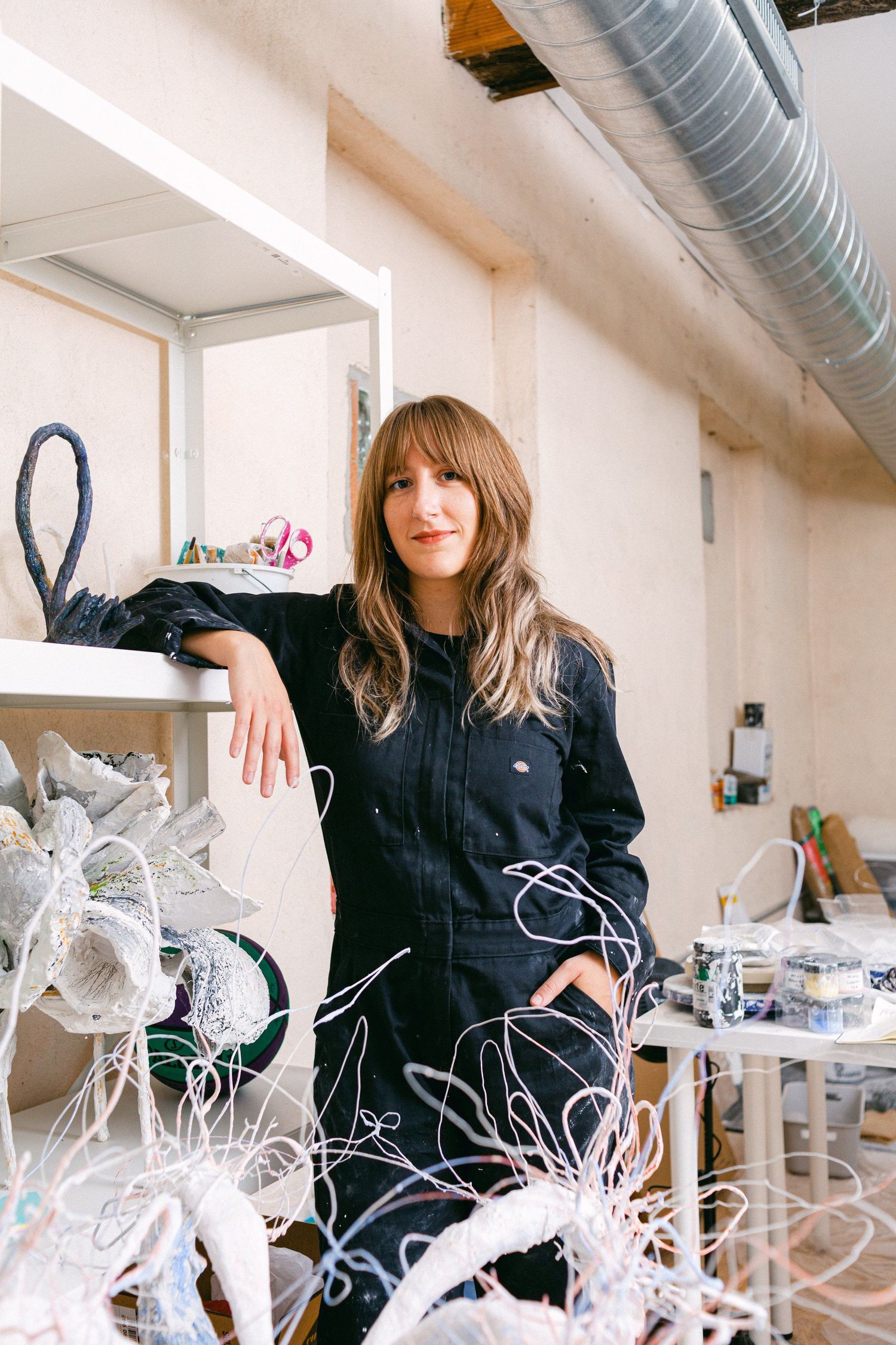 Artist works with delicate white wire sculptures in a bright studio space.