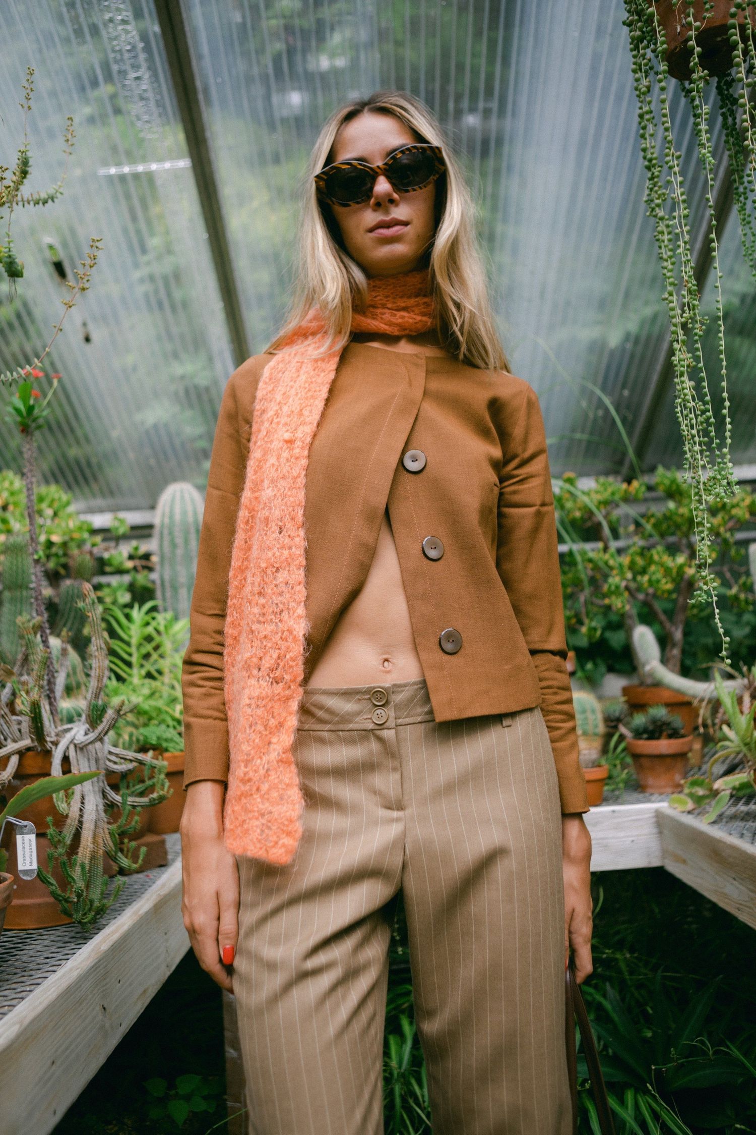 Fashion shots of brown coat and coral scarf styled in greenhouse setting.
