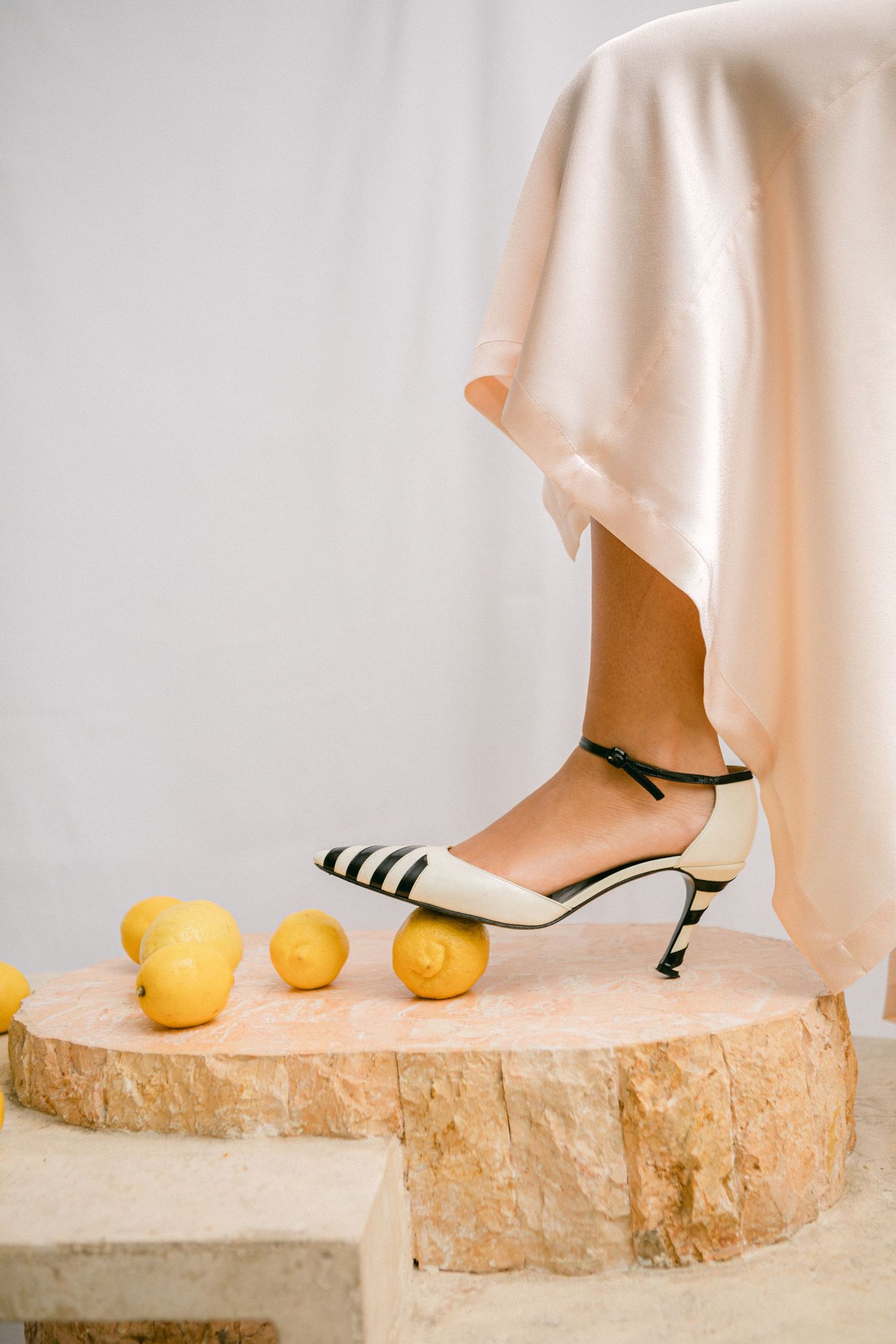 Artistic still life with white heels on stone pedestal and fresh lemons against light backdrop.