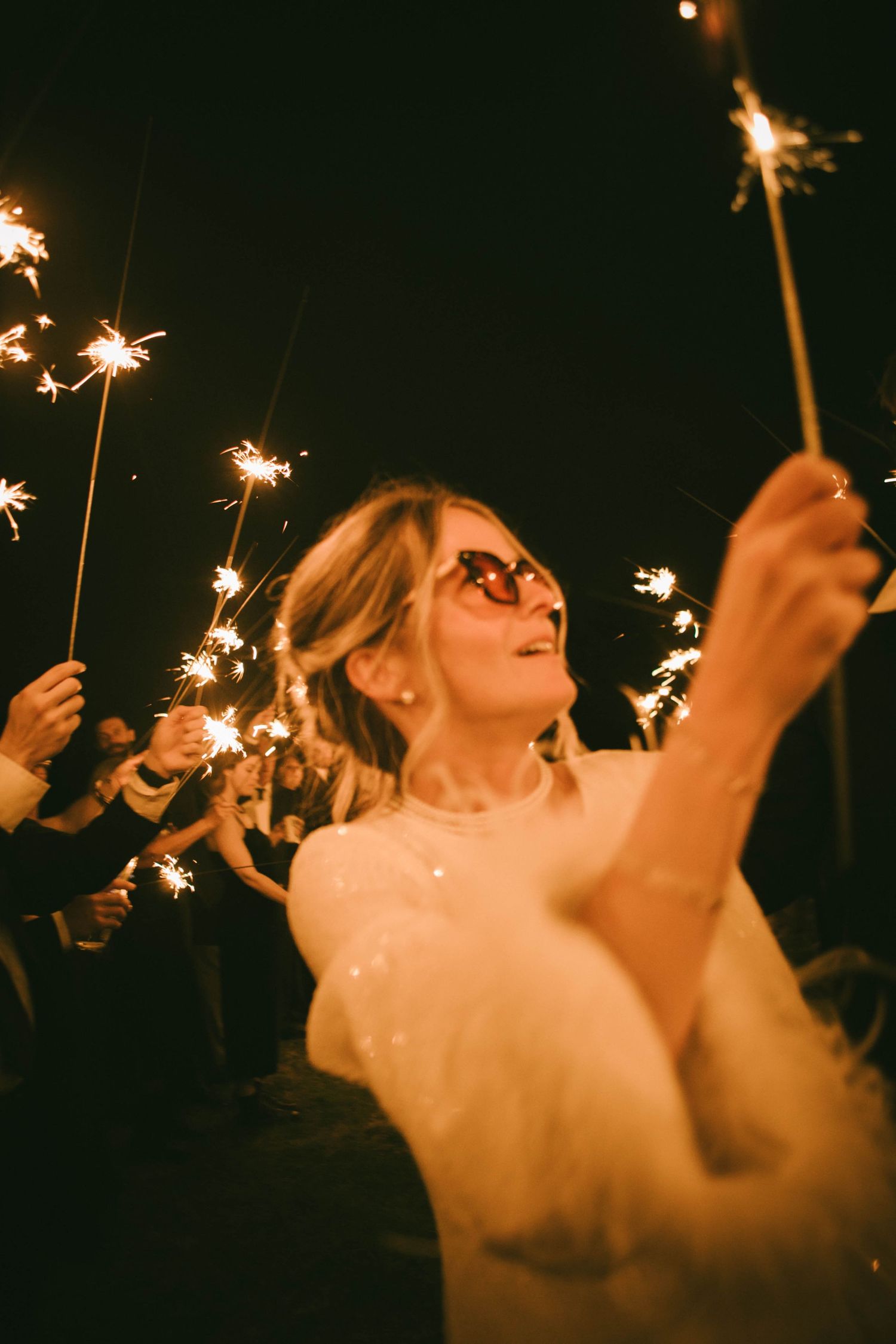 Wedding guests wave sparklers in celebration at night.
