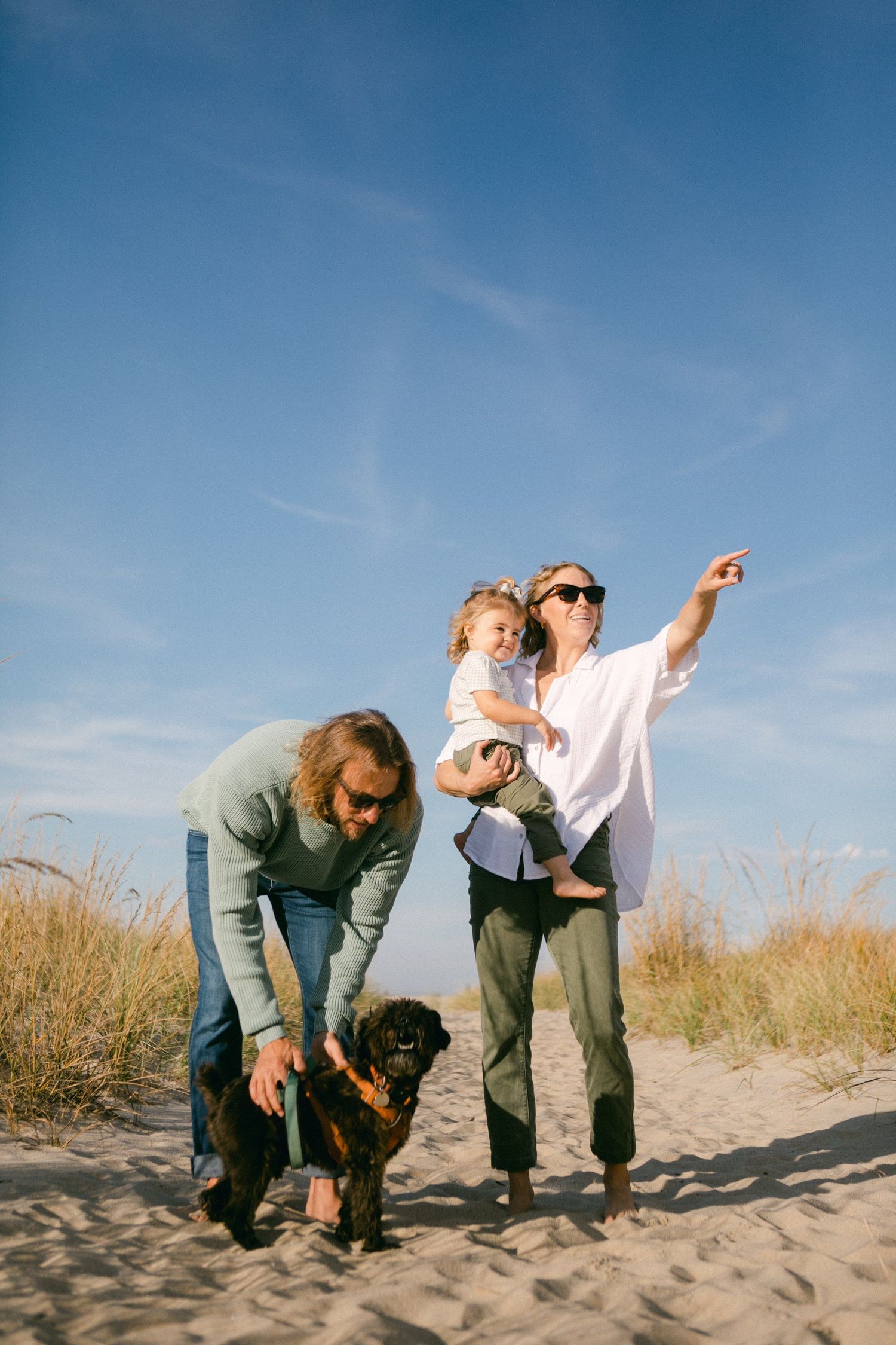 People playing and laughing together on a sandy beach under blue skies.