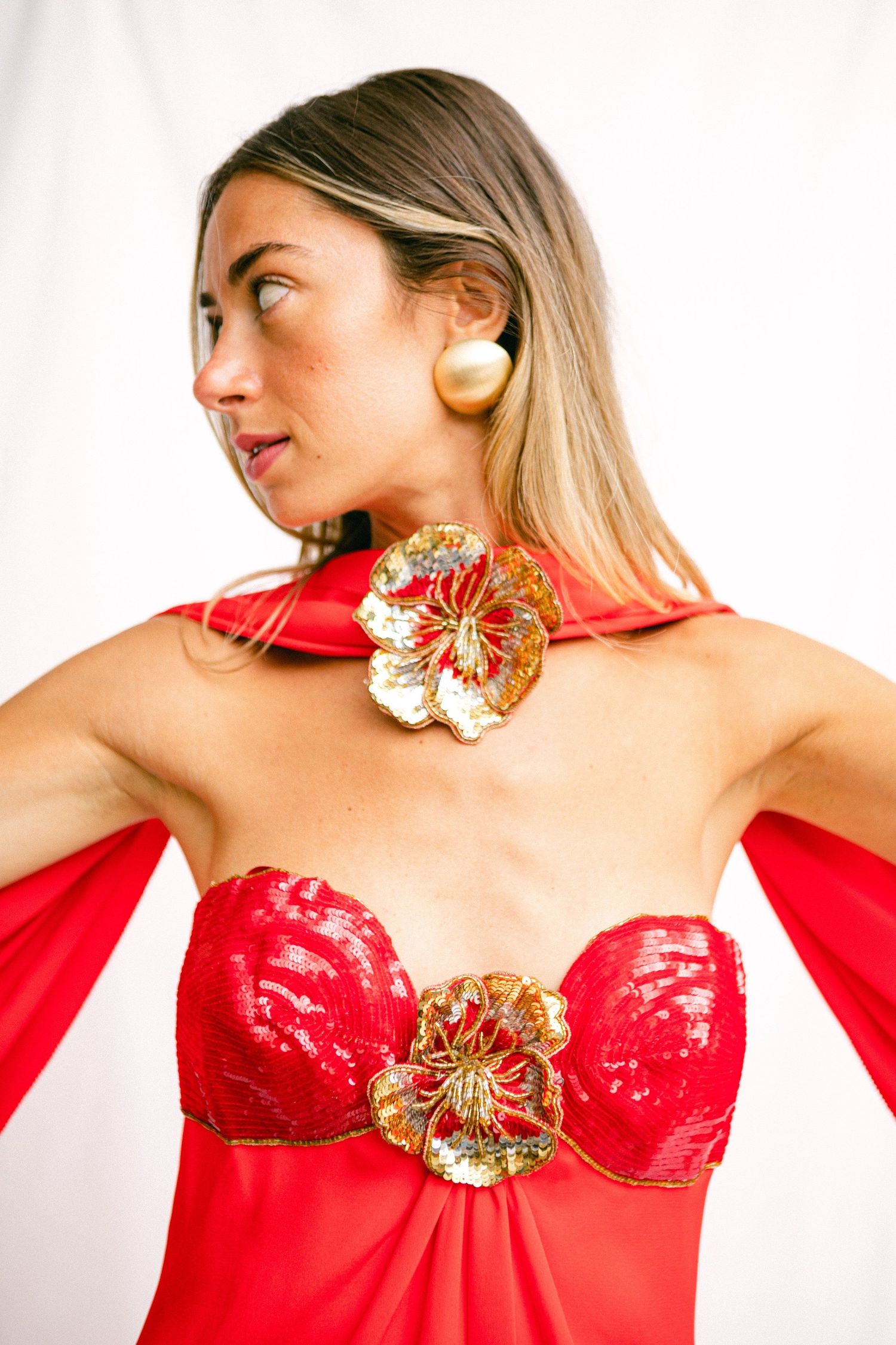 Dramatic poses in red formal dress with gold embellishments against white background.
