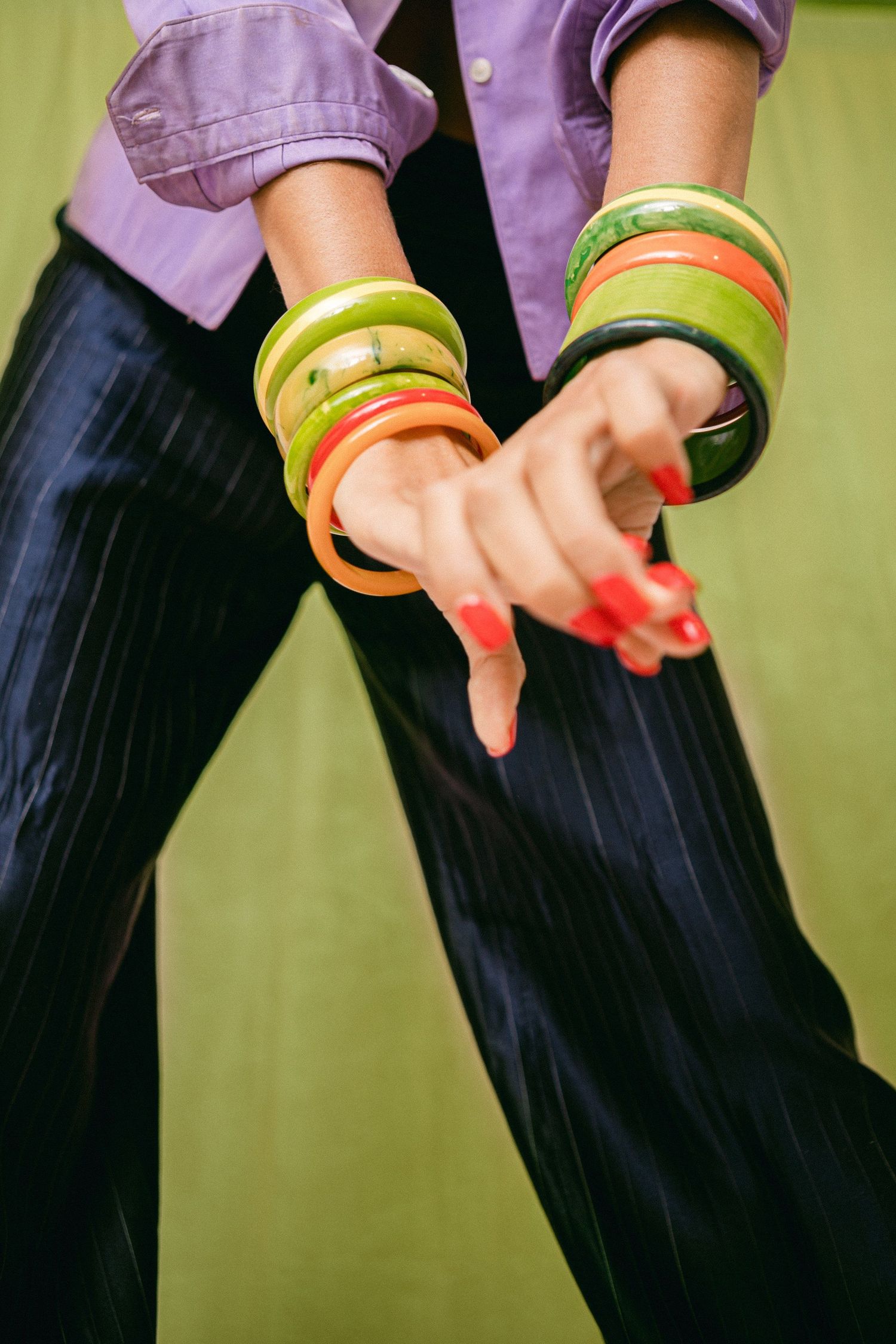 Colorful bangles and bracelets on arms against purple and green background.