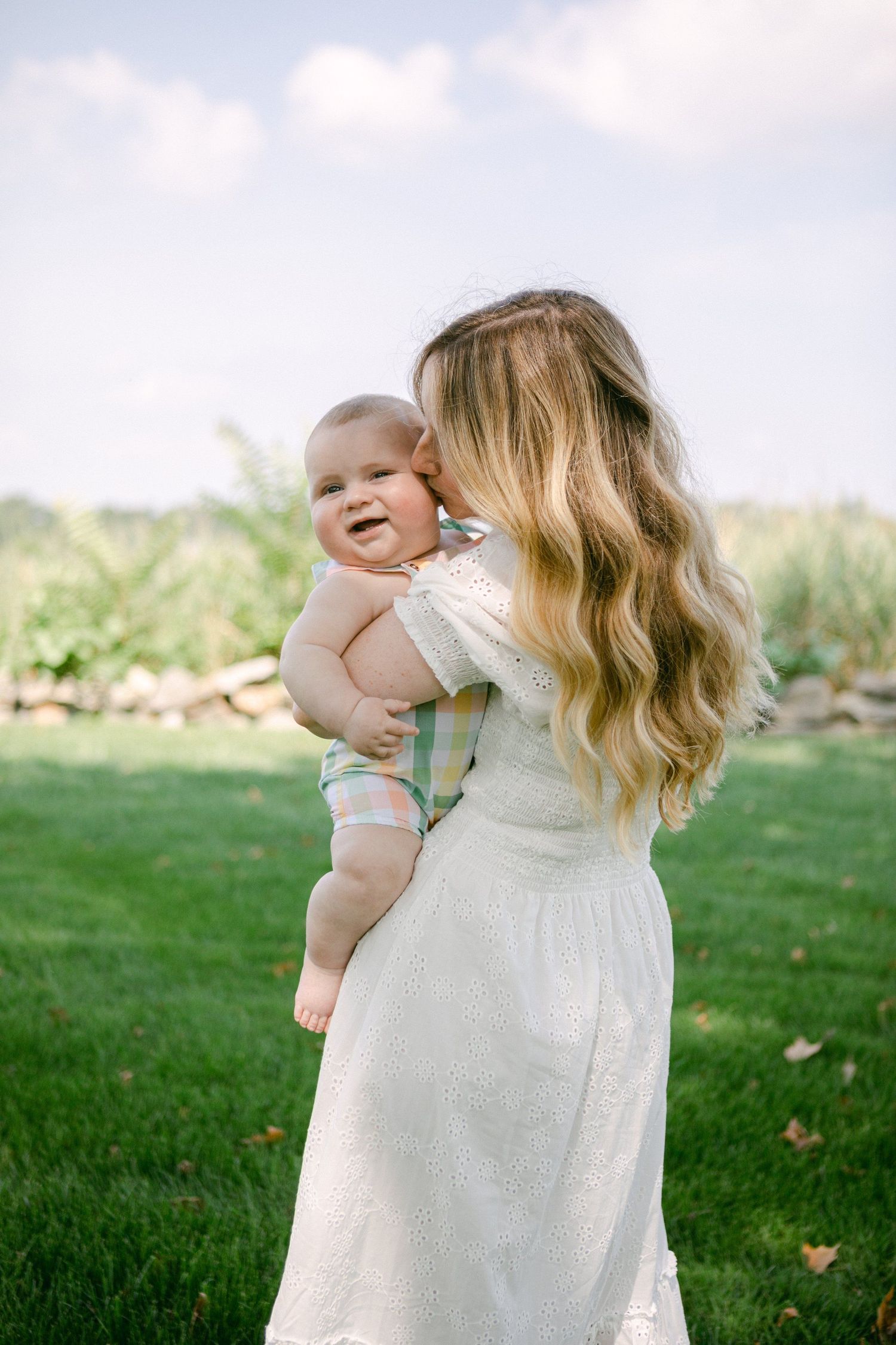 A tender moment captured outdoors with a baby being held against a grassy background.