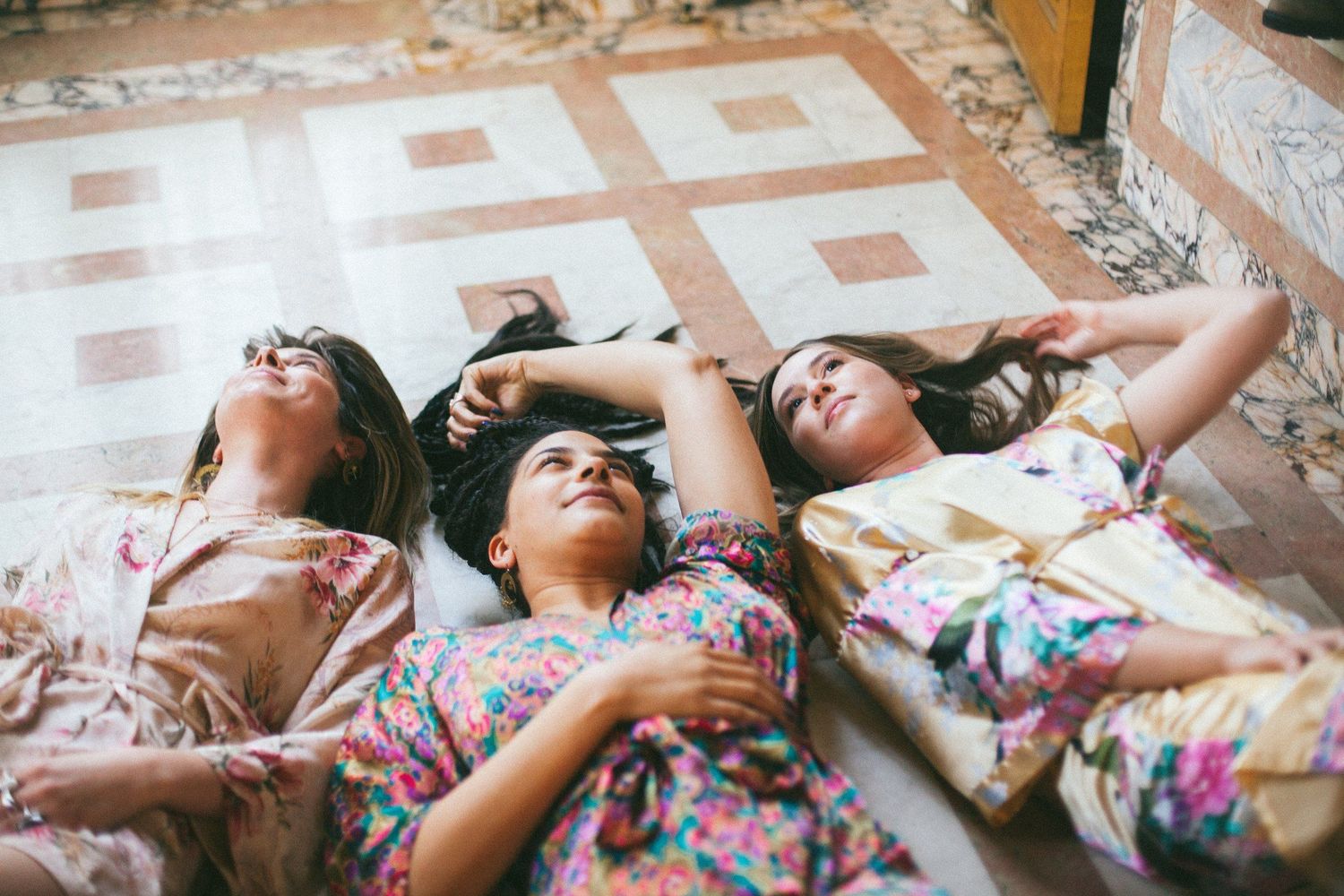 Friends lying down in a row on tiled floor wearing floral outfits.