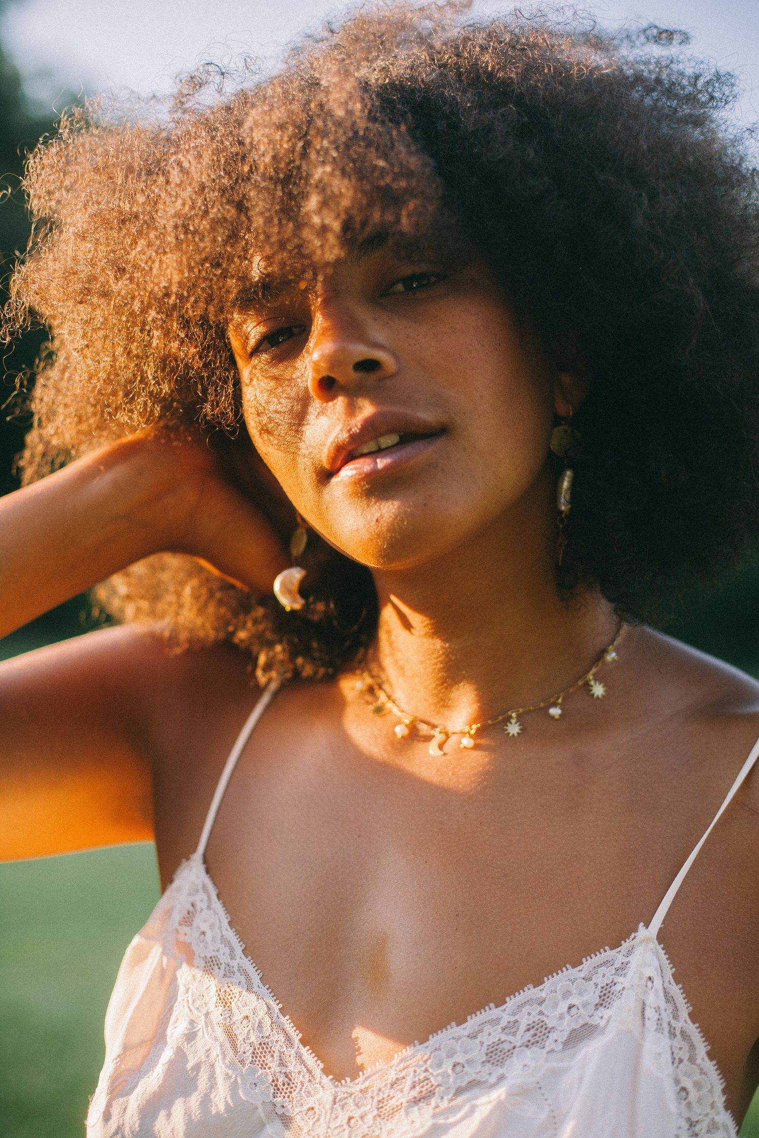 Close-up artistic portraits showing natural curly hair and delicate lace details in warm sunlight.