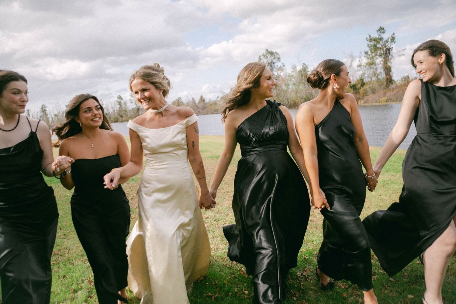 Wedding party holds hands in a line across a sunny field.