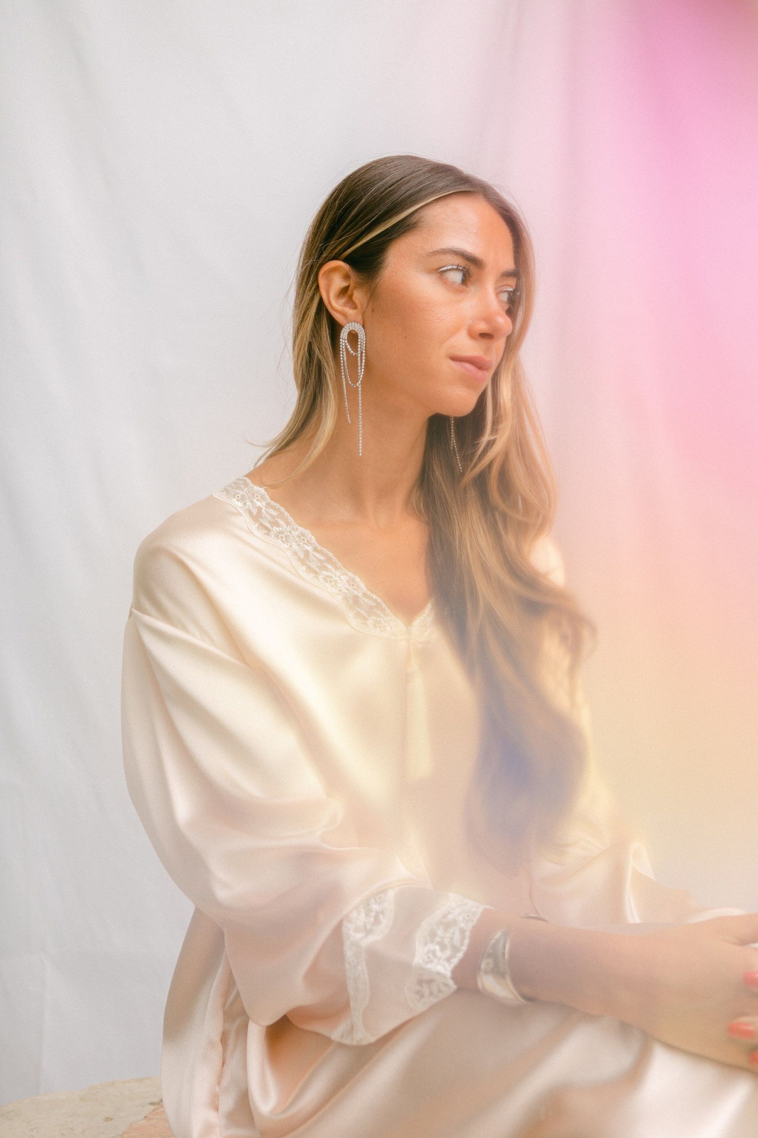 Ethereal portraits in flowing white silk blouse against pink gradient background.