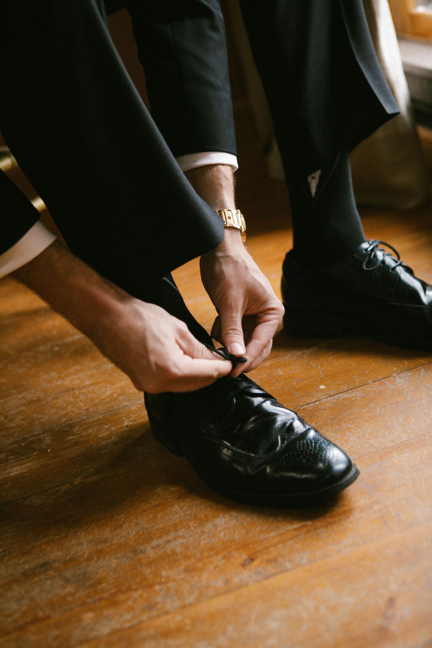 Series of shots showing hands tying formal black dress shoes on wooden floor.