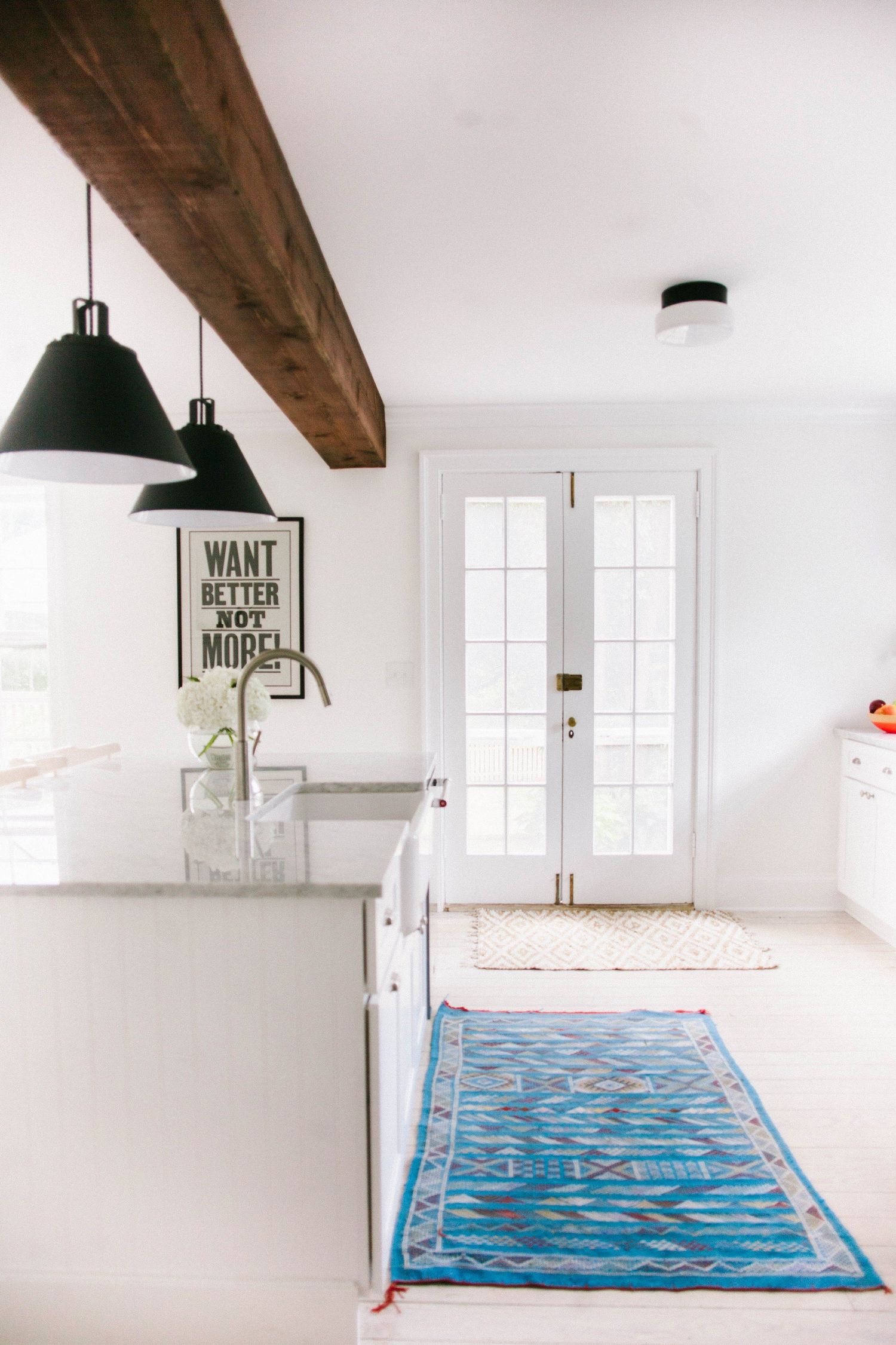 Minimalist white room interior with exposed wooden beams and blue area rug.