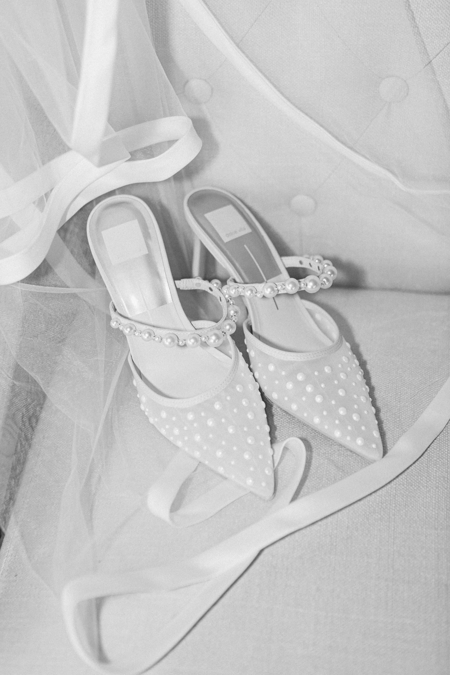 Delicate white polka dot bridal shoes with pointed toe displayed on tulle fabric.