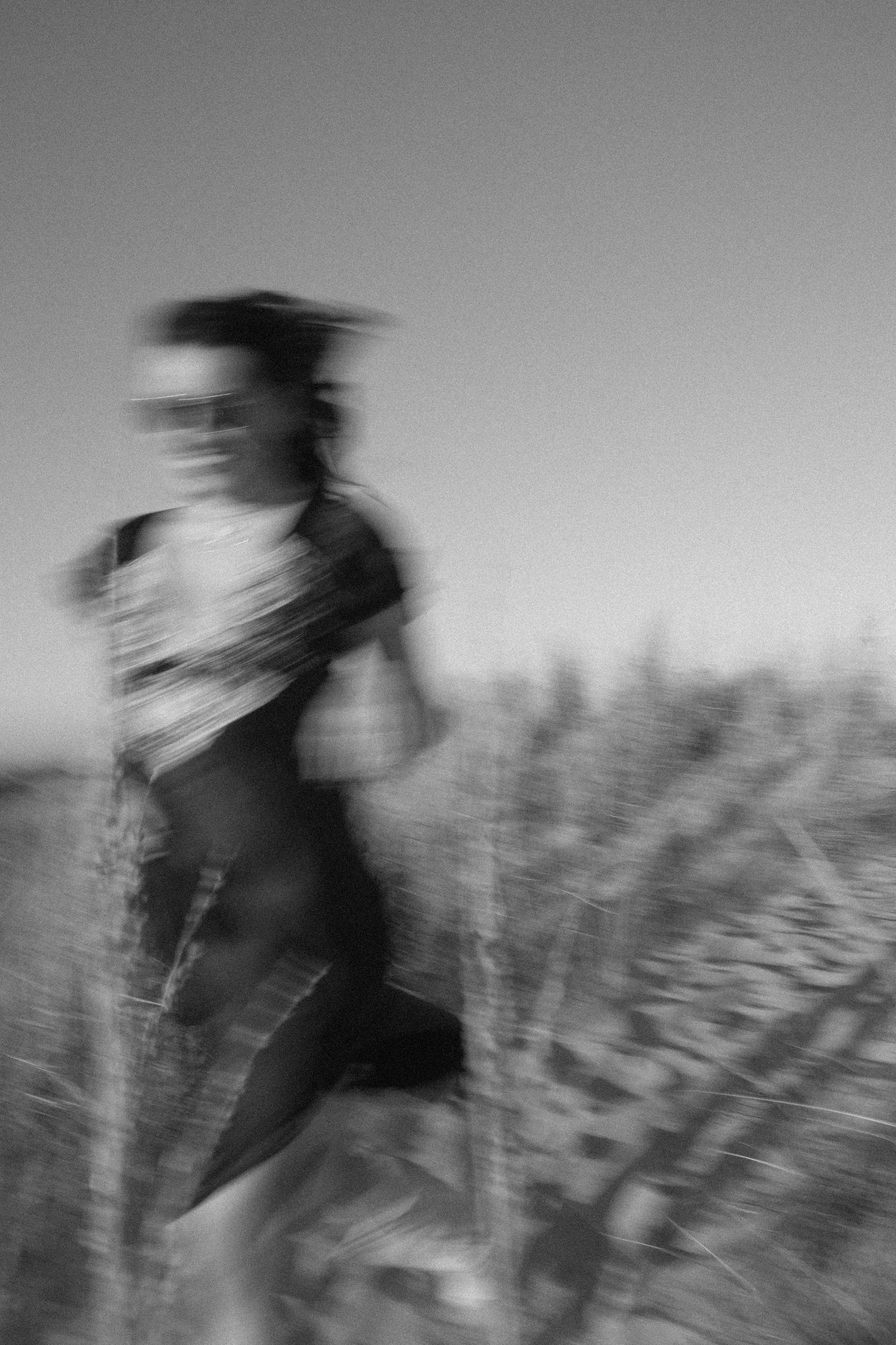 Black and white motion blur sequence of a figure moving through tall grass in a field.