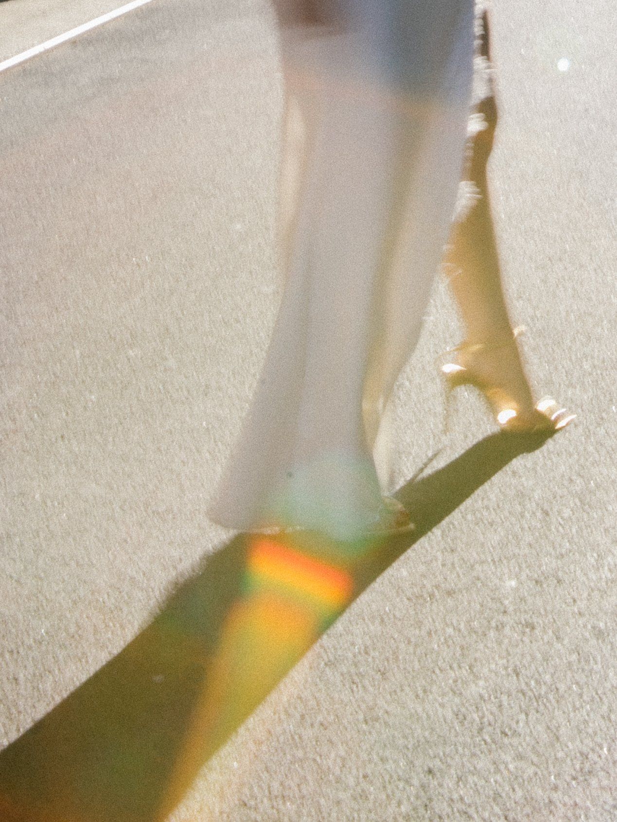 Artistic shot of feet and shadows on pavement with sunlight creating rainbow lens flares.