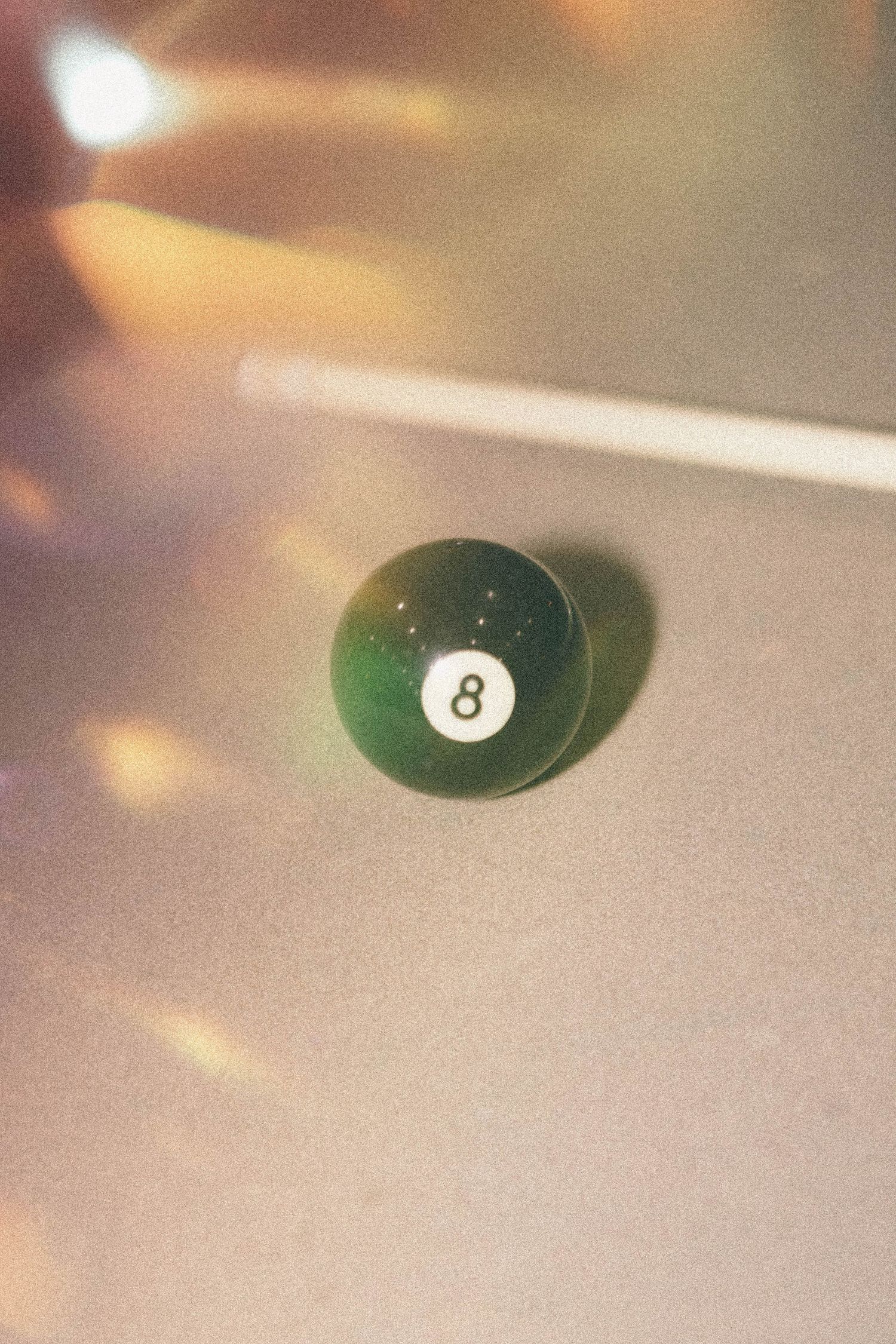 Green number 8 pool ball photographed with soft focus and light flares.