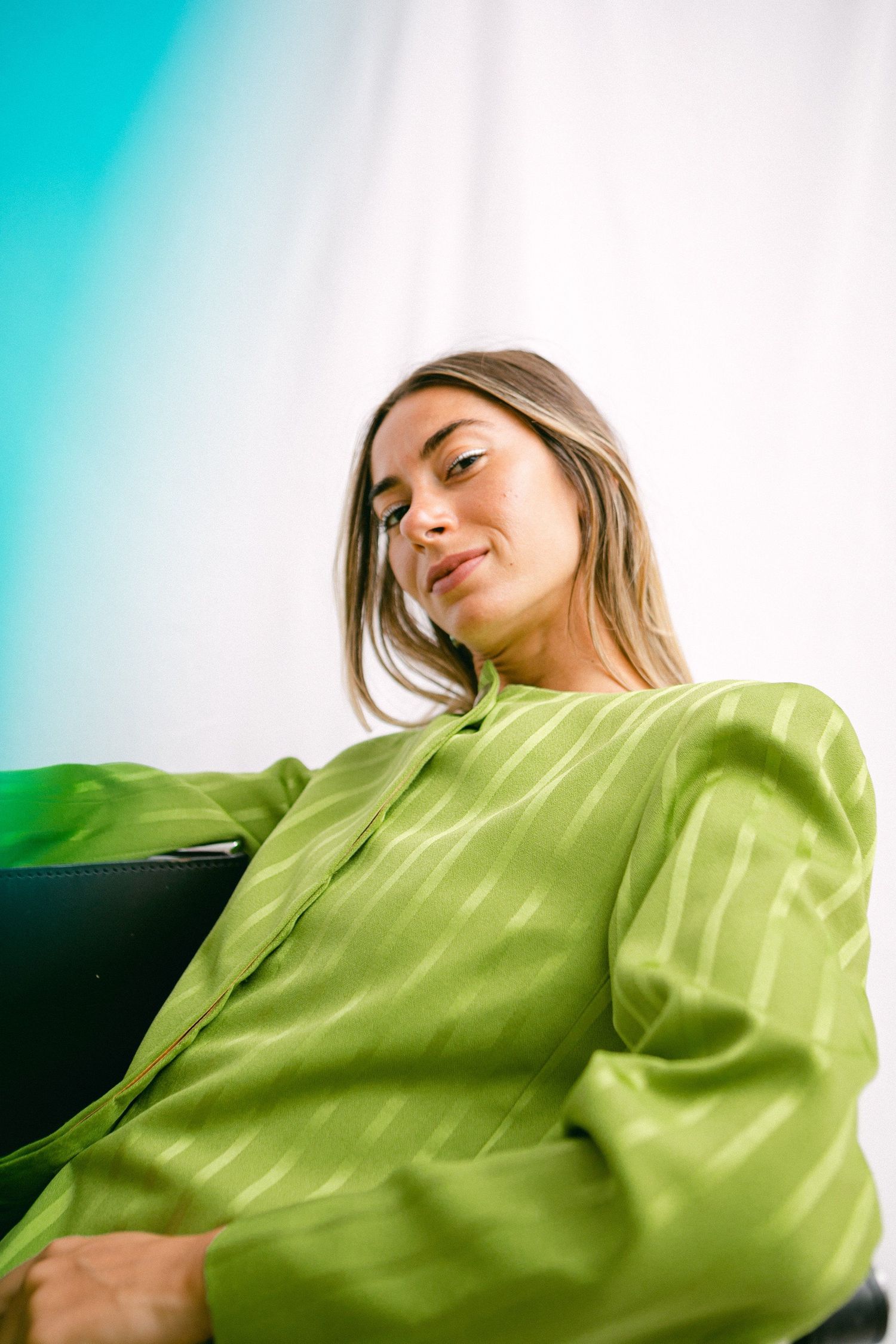 Person wearing lime green satin shirt lying down against blurred background.
