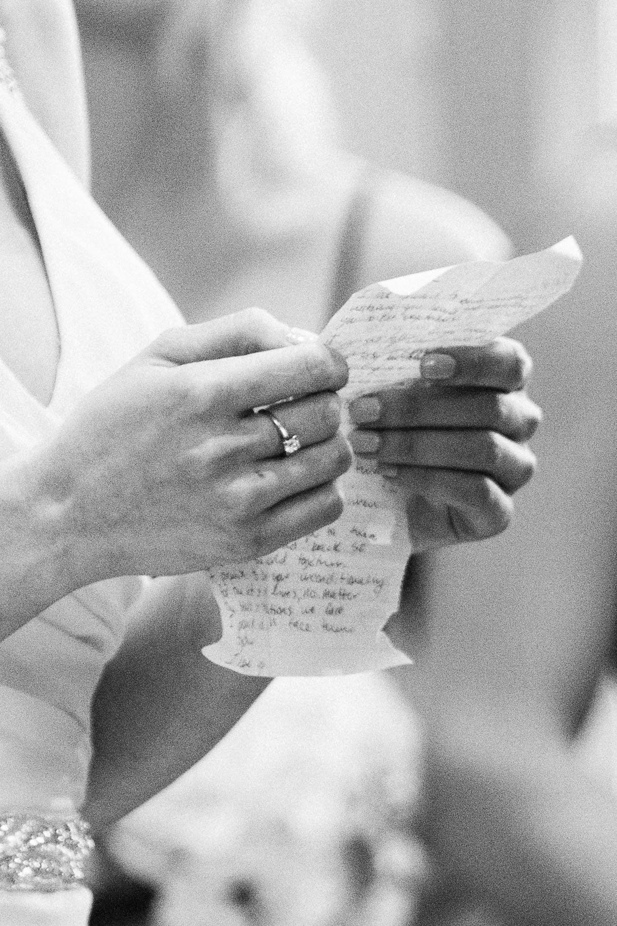 Close-up of hands holding handwritten wedding vows in black and white.