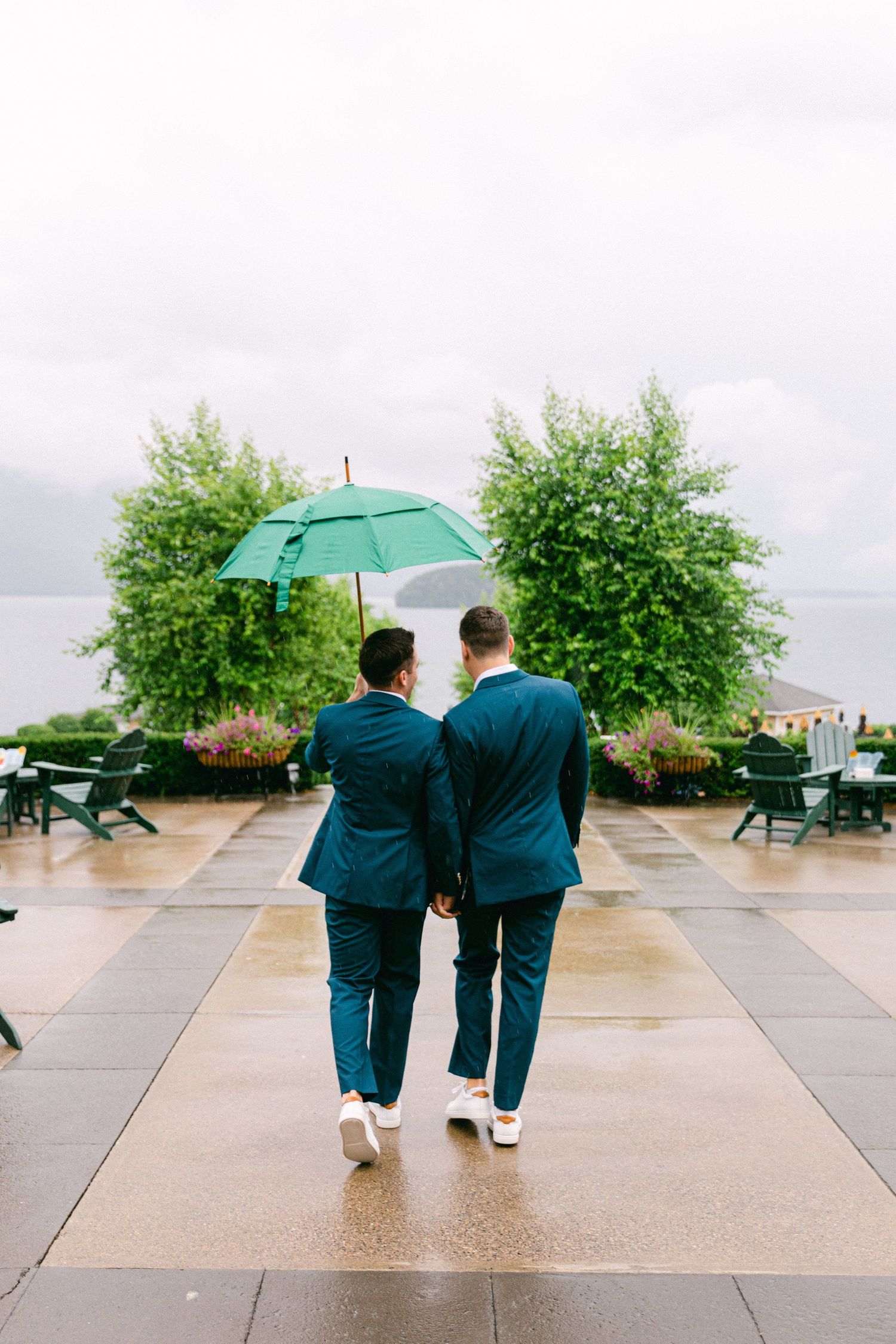 Two people walking with a green umbrella on a rainy day across concrete plaza.