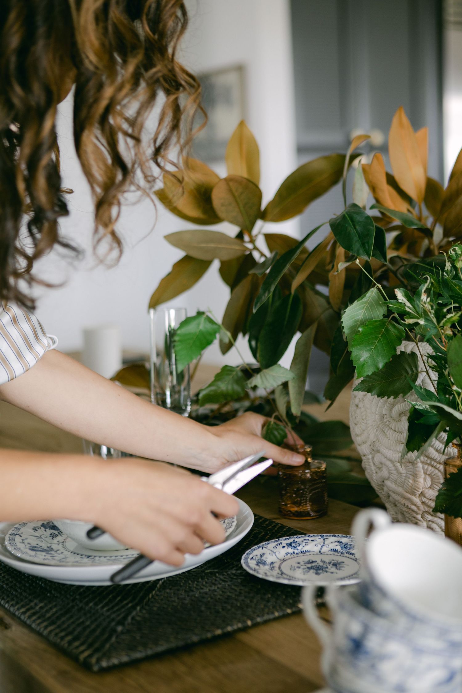 Hands arranging greenery and decorative items on a dark placemat in a series of styled vignette shots.