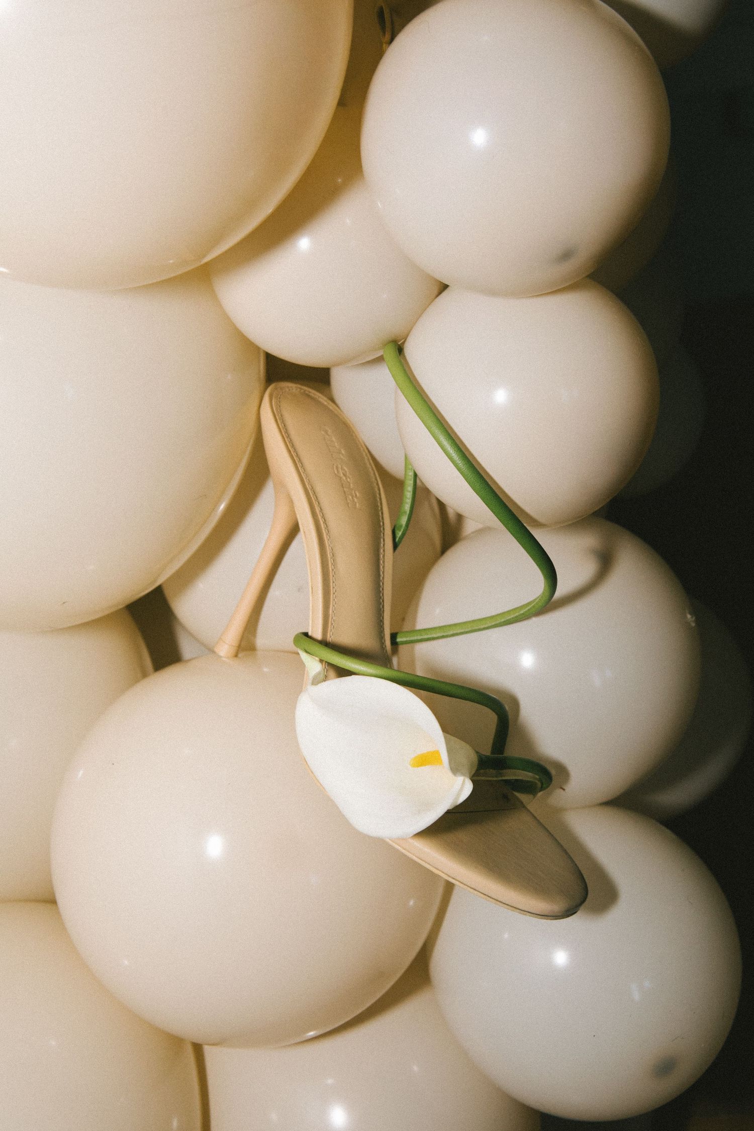Gold strappy heeled mule with white calla lily resting on cream balloons.