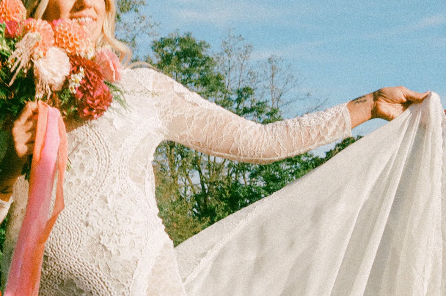 Close-up detail of delicate white lace wedding dress fabric against a natural outdoor backdrop.