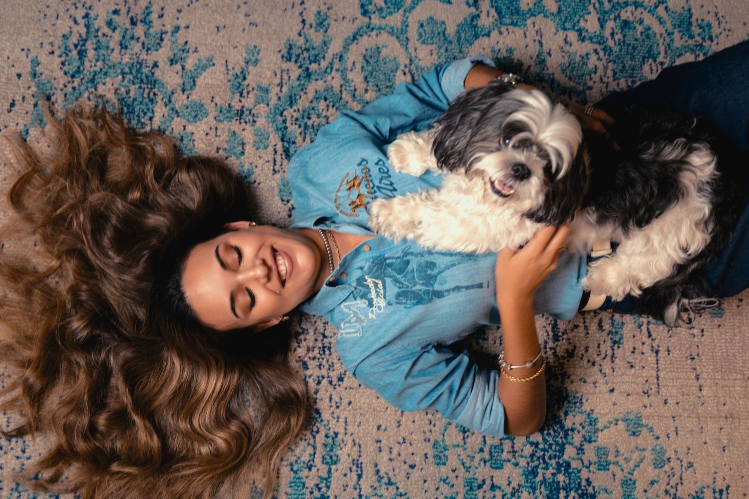 A figure in a blue dress lies gracefully on a beige textured surface with hair elegantly spread out.