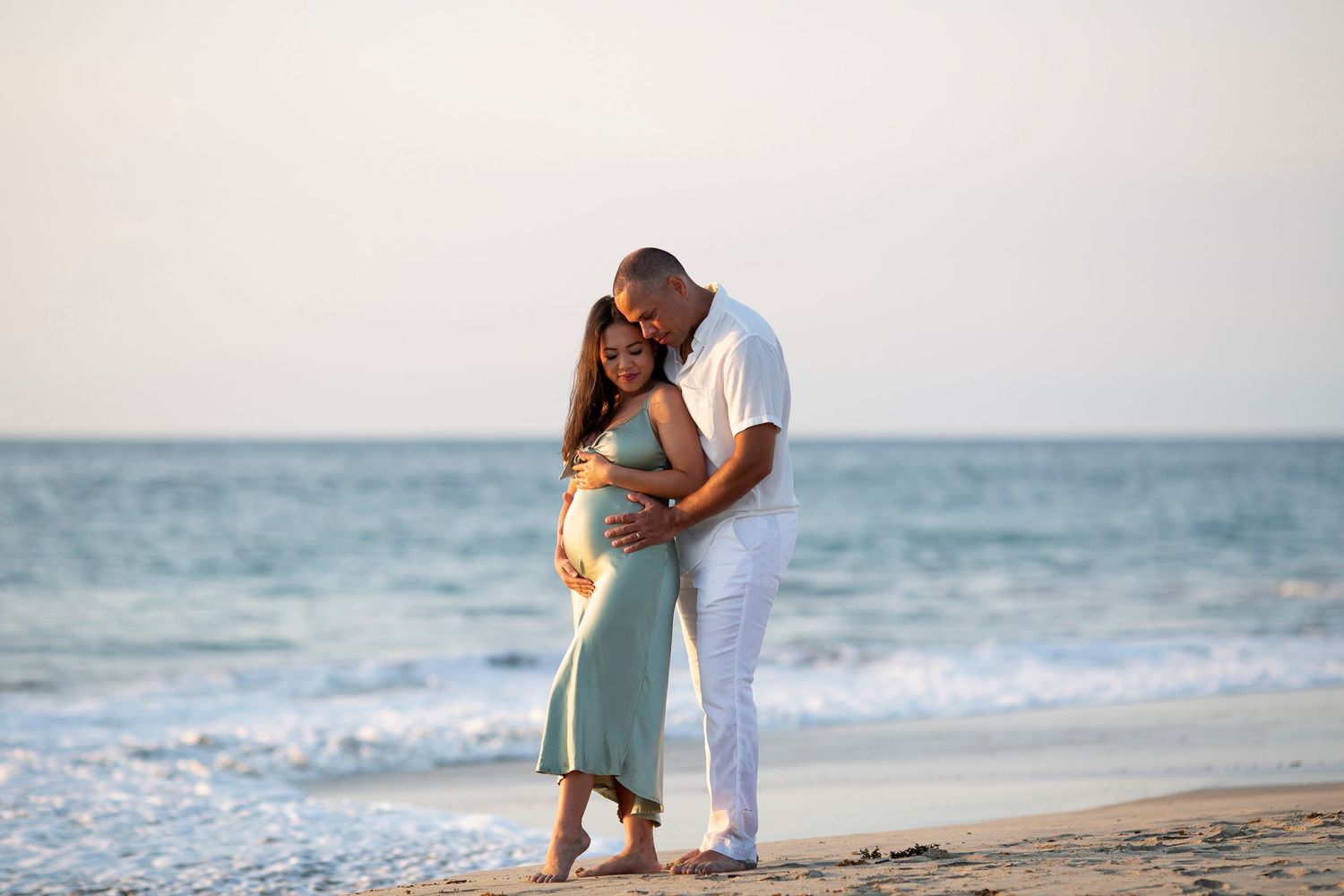Beach maternity photography session at Conrad Punta de Mita, Mexico, capturing an expectant couple embracing by the ocean.