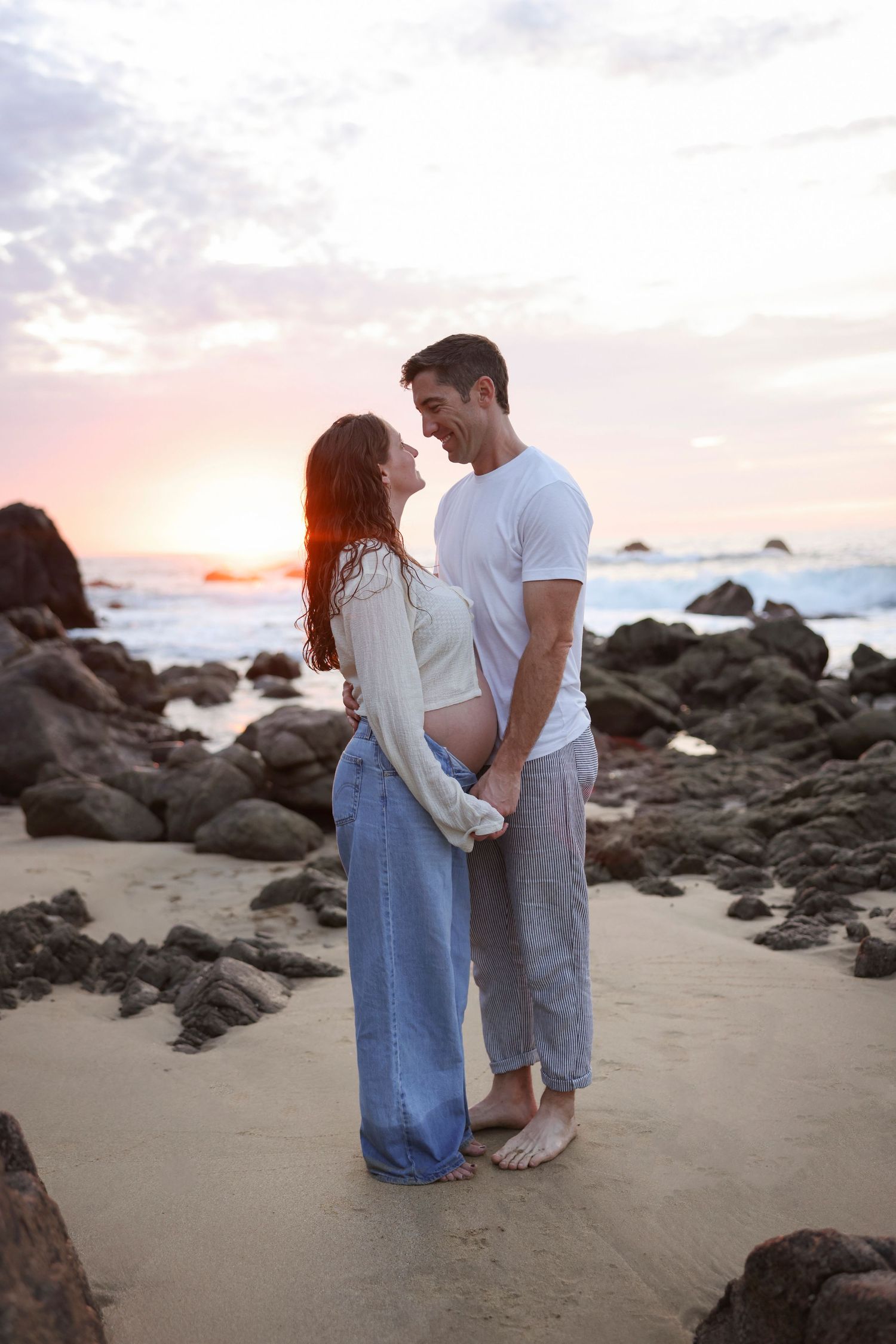 Maternity sunset photography in Sayulita, Mexico, capturing a romantic moment among the rocks by the ocean.