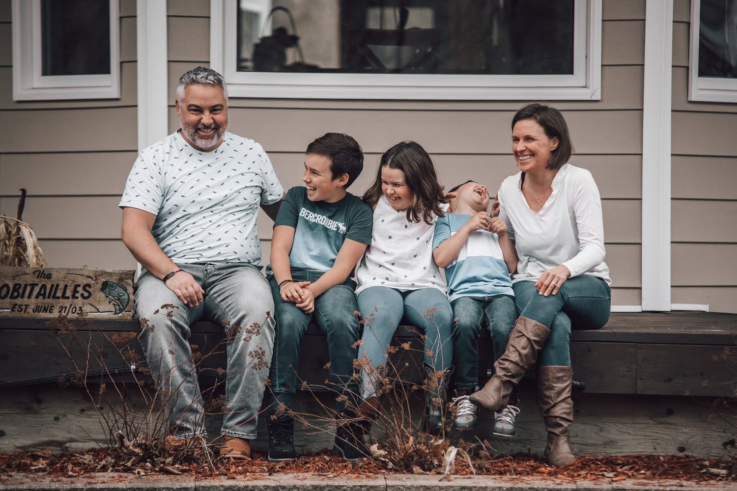 Happy family of five sitting on front porch steps, laughing together on an autumn day.