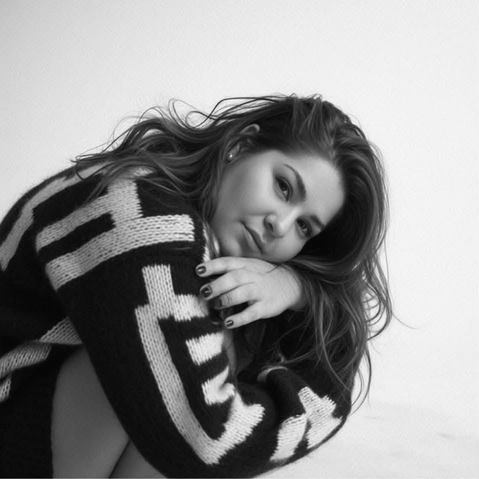 Black and white photo of a young woman posing in a bold patterned knit sweater with flowing hair.